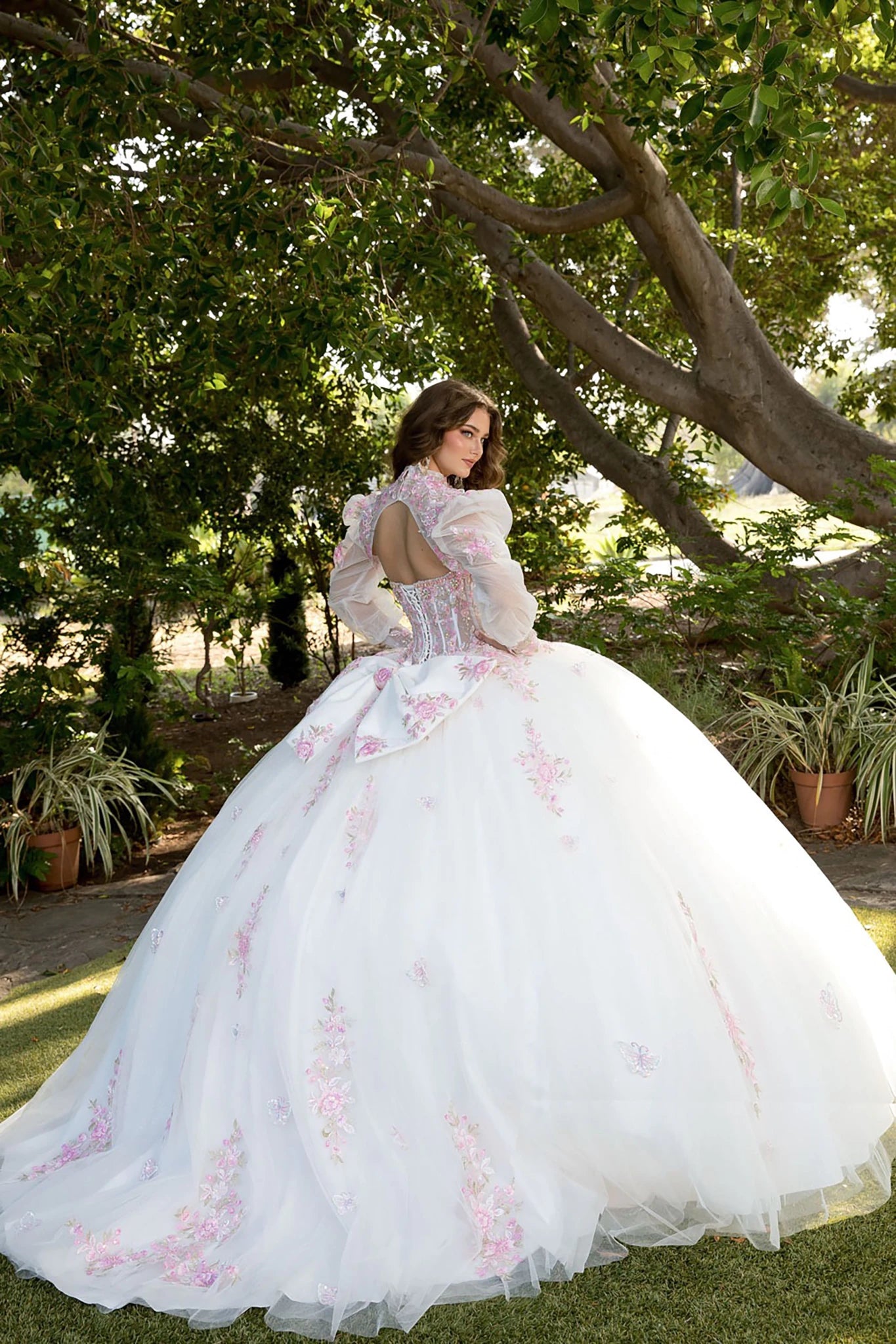 Back view of a woman wearing a white quinceañera dress with floral details and corset bodice