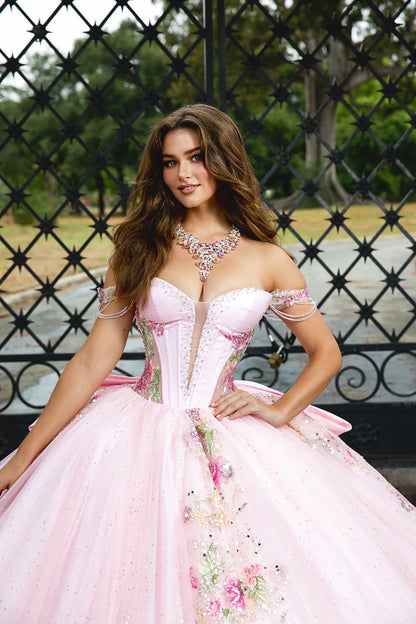 Woman in a pink formal gown with floral details sitting outdoors.
