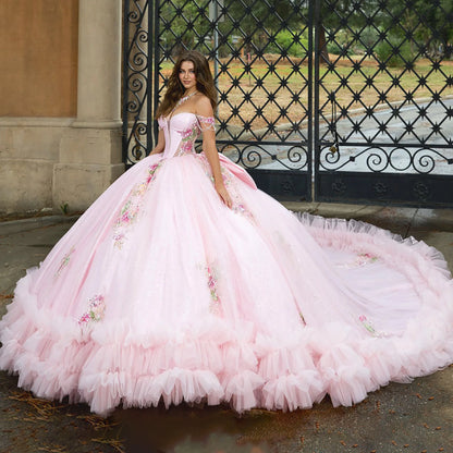 Pink ball gown with floral details worn by a model in front of an ornate gate.