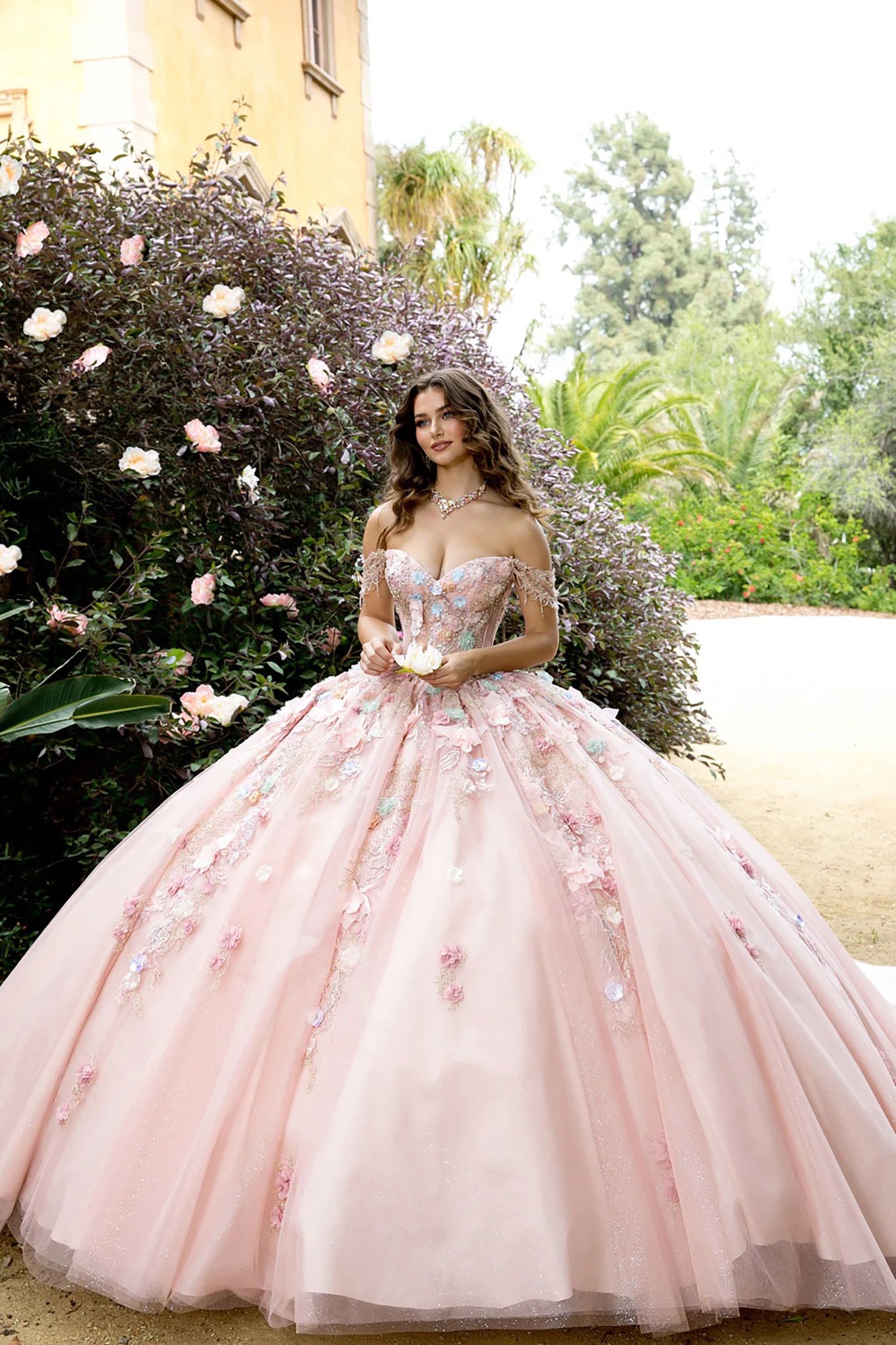 Front view of a woman wearing a pink quinceañera dress with floral details, corset bodice and layered skirt