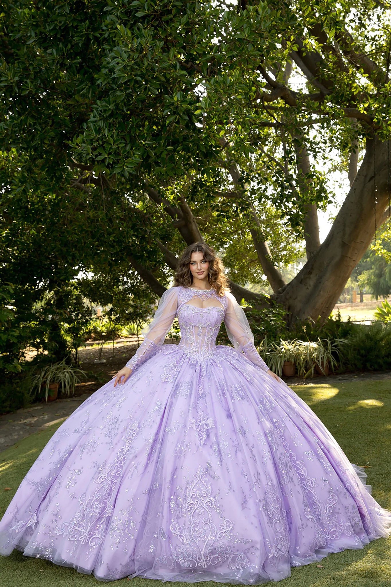 Front view of a woman wearing a lilac quinceañera dress with glitter tulle skirt, embroidered see-through bodice and matching bolero jacket