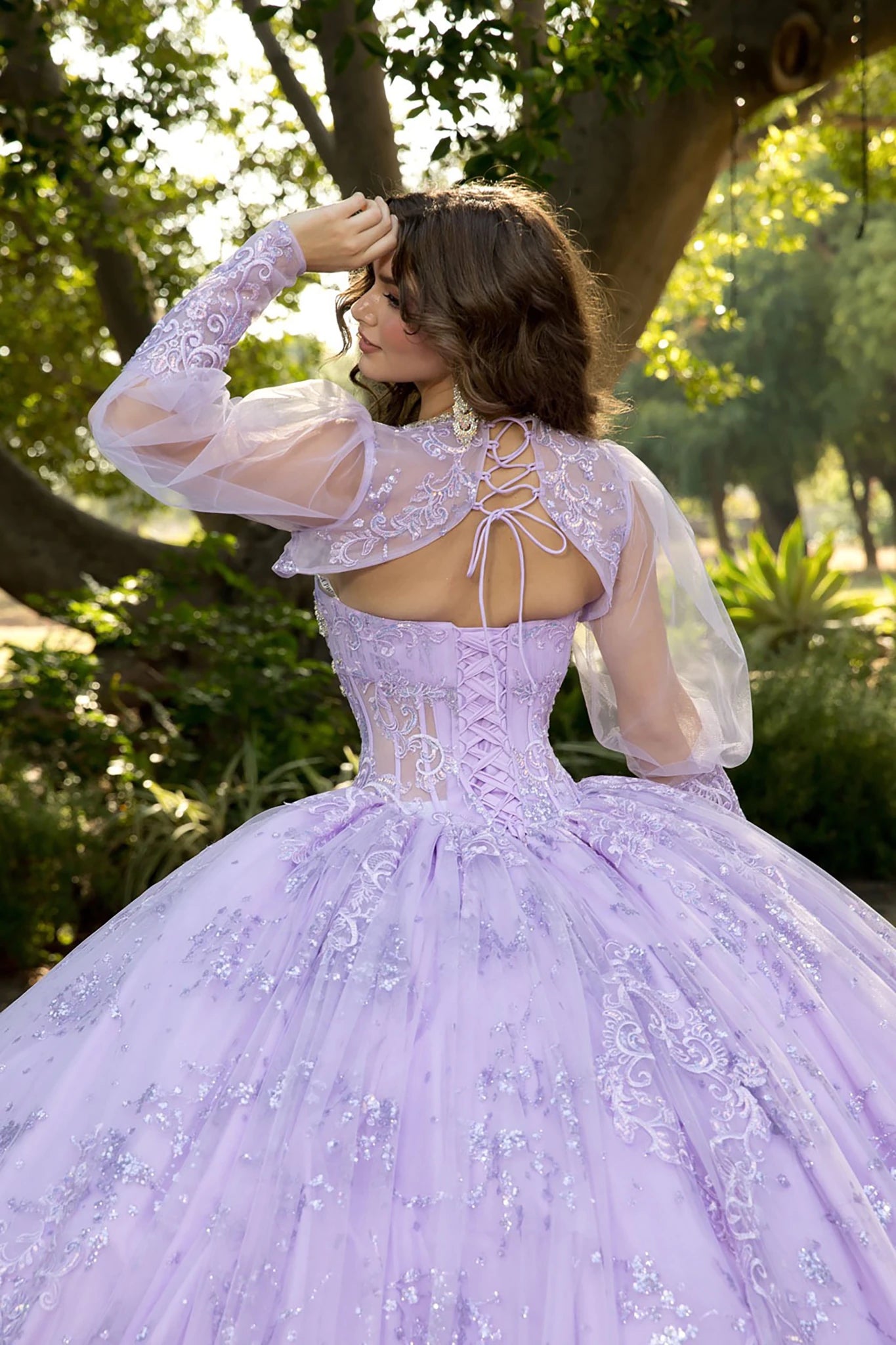 Back zoom view of a woman wearing a lavender quinceañera dress with floral details, corset bodice and tulle skirt