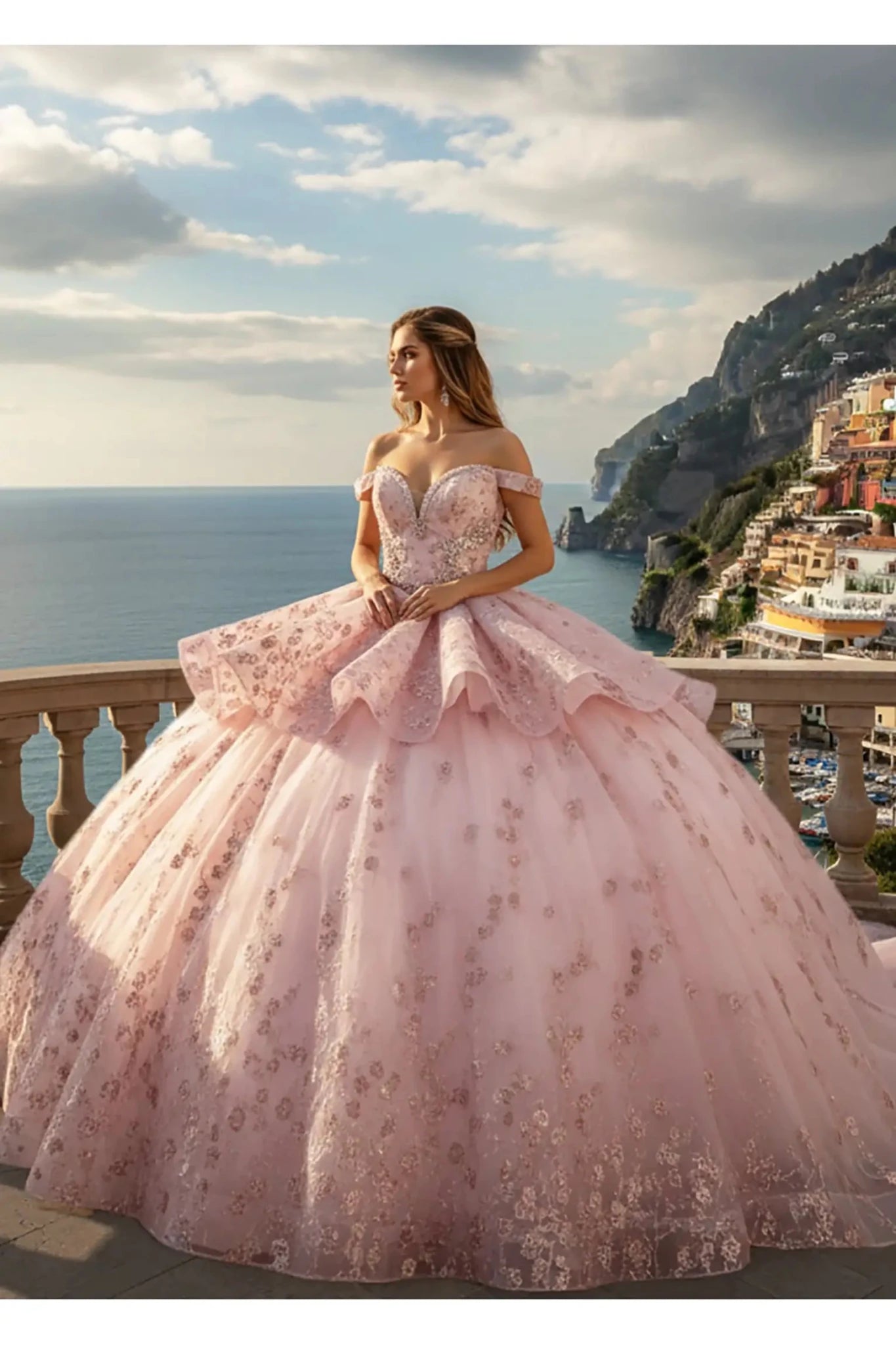 Full view of a pink ballgown with an off-the-shoulder neckline and a tiered peplum waist, decorated with shimmering floral embroidery and crystal accents against a coastal sea horizon.