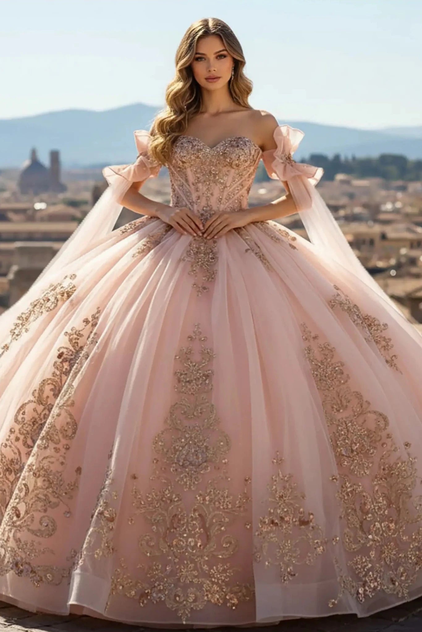 Woman with long blonde hair wearing a Rose Gold off-the-shoulder ball gown with intricate floral embroidery, standing on a stone balcony overlooking a lush green vineyard under a clear blue sky.