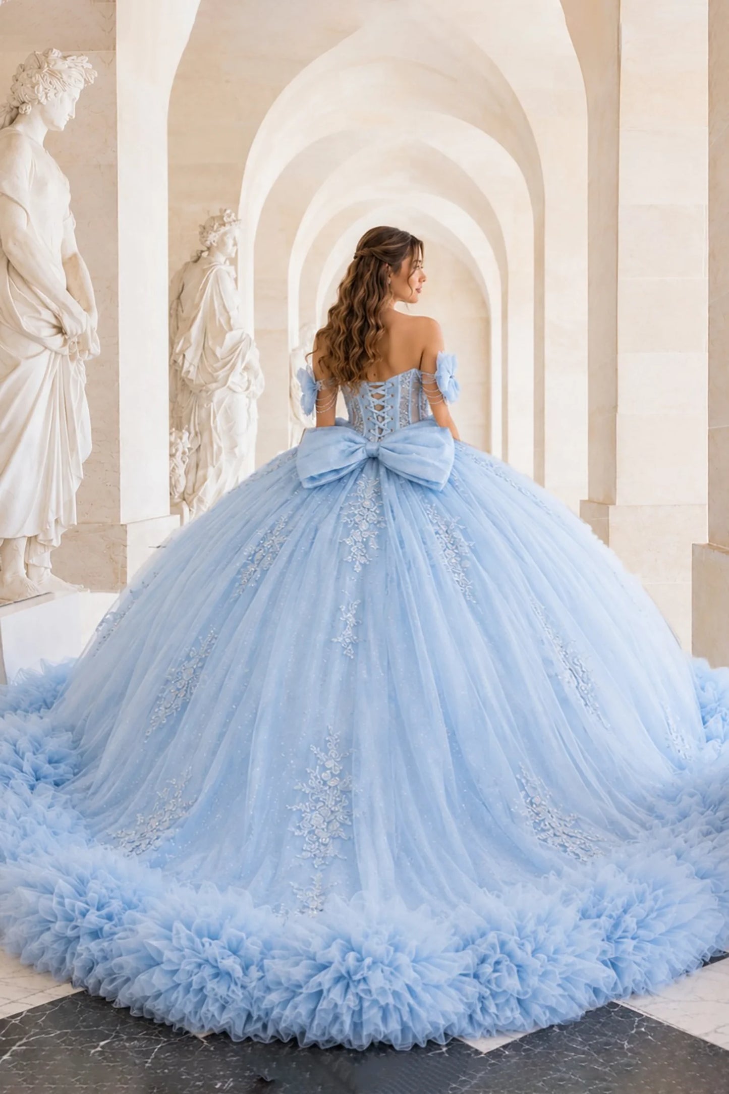 Light blue quinceañera ball gown with lace-up back, oversized statement bow, ruffled hem and delicate floral details