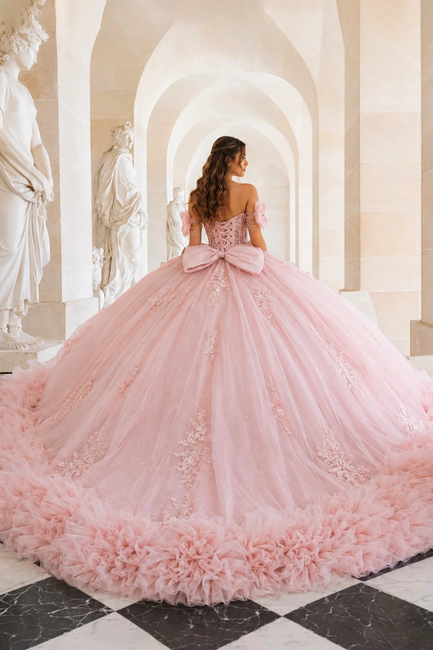 Pink quinceañera ball gown with lace-up back, oversized statement bow, ruffled hem and delicate floral details