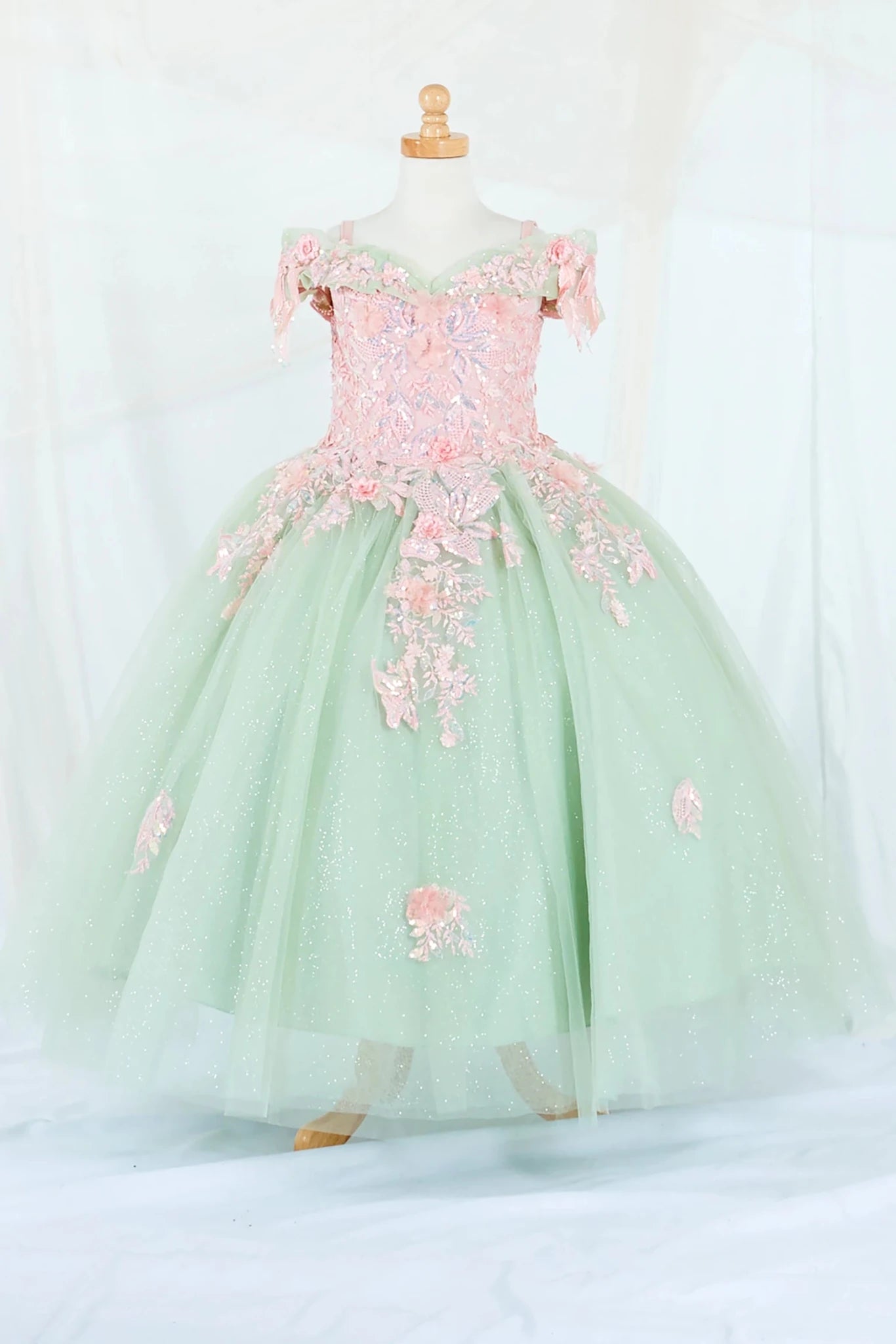 Front-facing display of an elegant sage and blush ball gown featuring a fitted bodice, detachable bow accent, and a glitter tulle layered skirt.