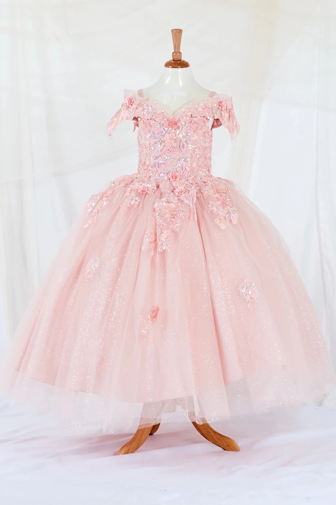 Front-facing display of an elegant blush ball gown featuring a fitted bodice, detachable bow accent, and a glitter tulle layered skirt.