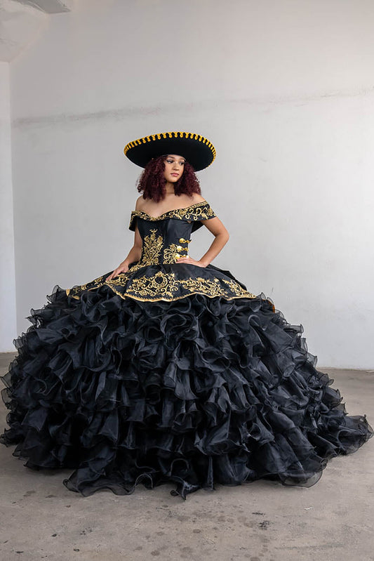Woman wearing a black and gold elaborate dress with a matching hat in an indoor setting.