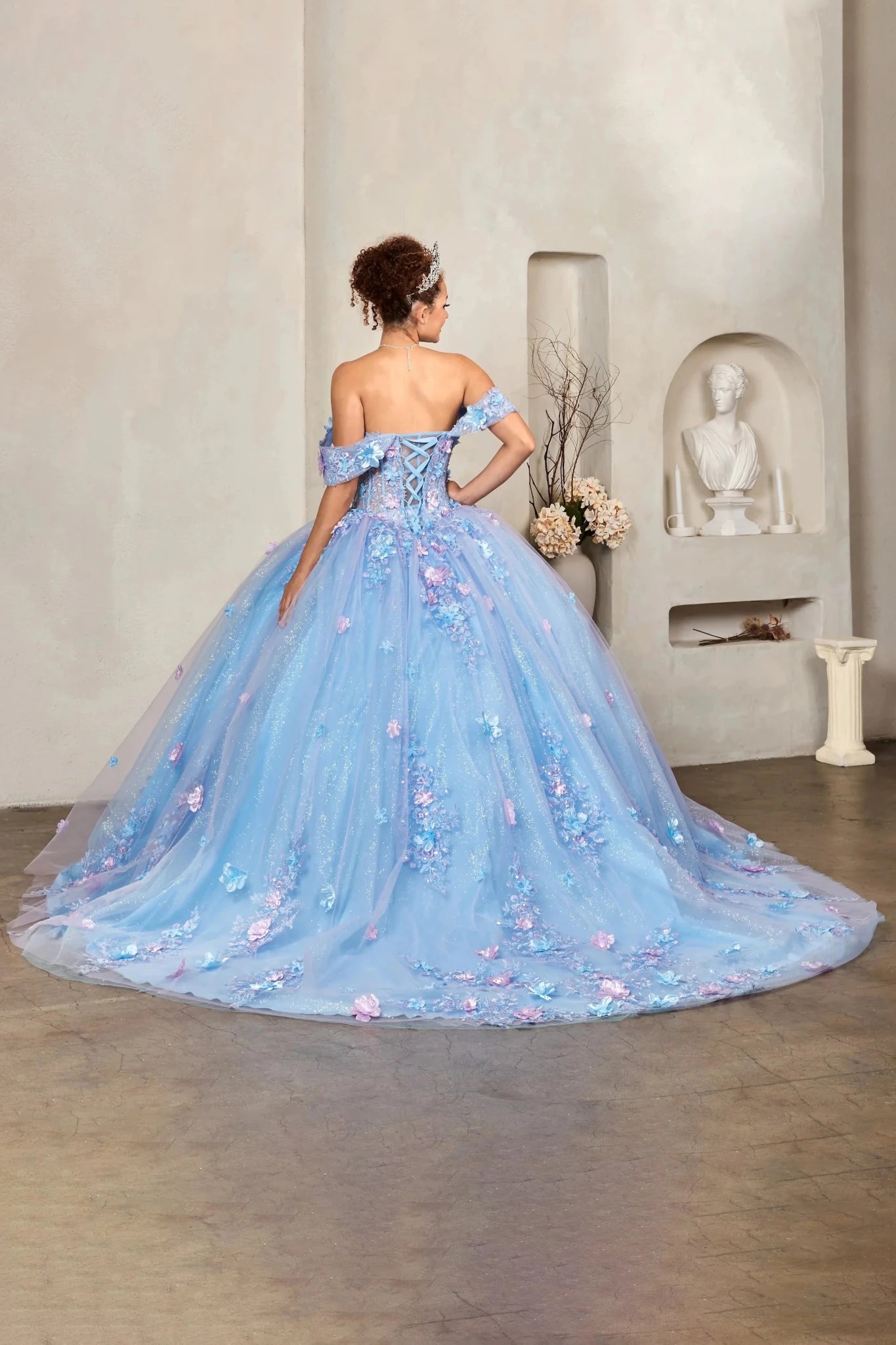 Girl in a light blue Quinceanera ball gown with lilac floral details in an indoor setting.