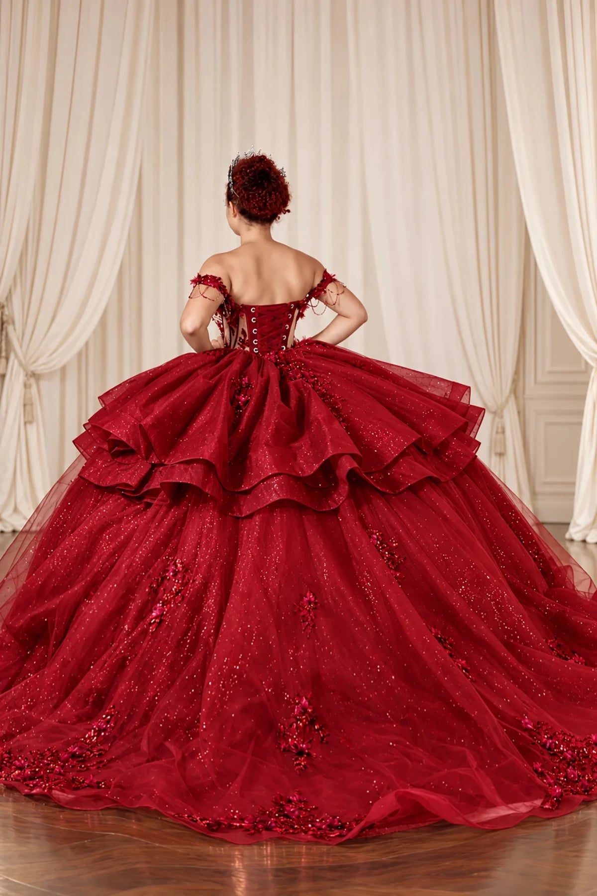 Back of the burgundy quinceañera ball gown showing lace-up corset closure and layered ruffle skirt.