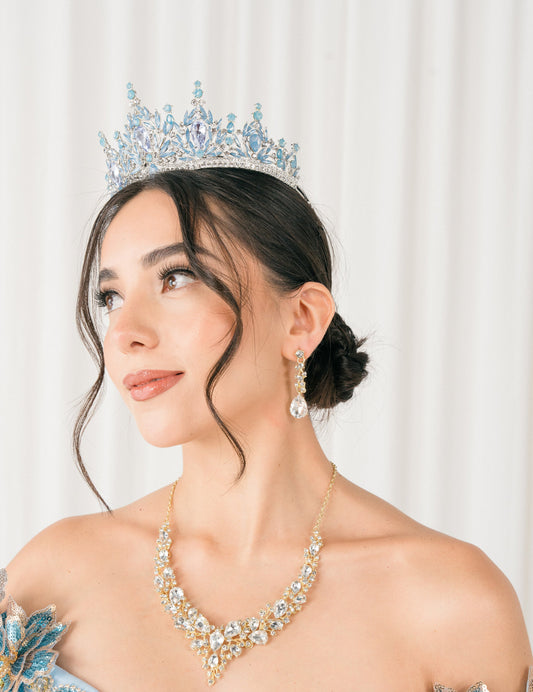 Woman wearing a sky blue tiara and formal gown with jewelry against a white background