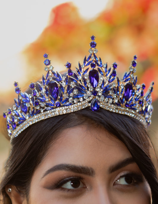 a girl wearing a royal blue and gold tiara with a blurred colorful background