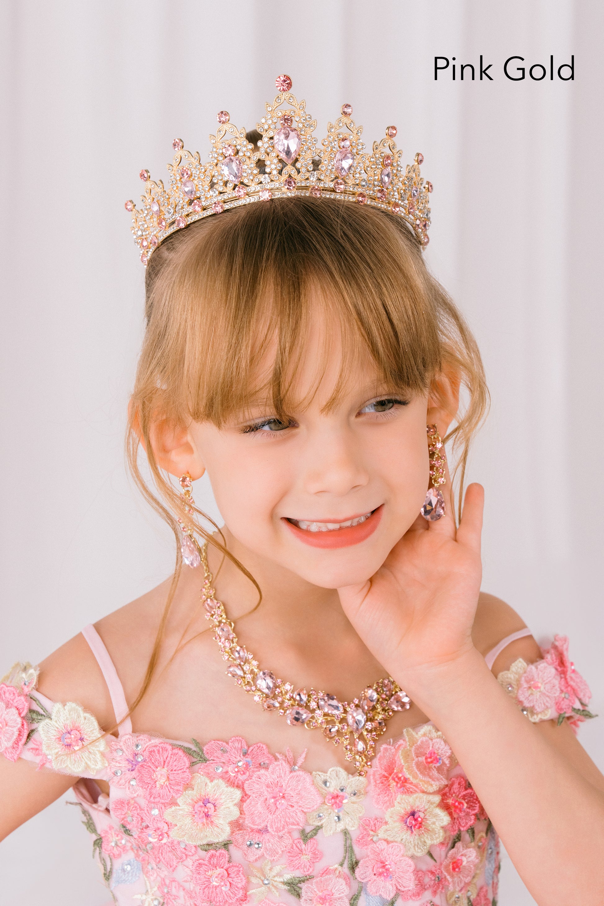 Young girl wearing a pink gold tiara and matching dress with floral details.
