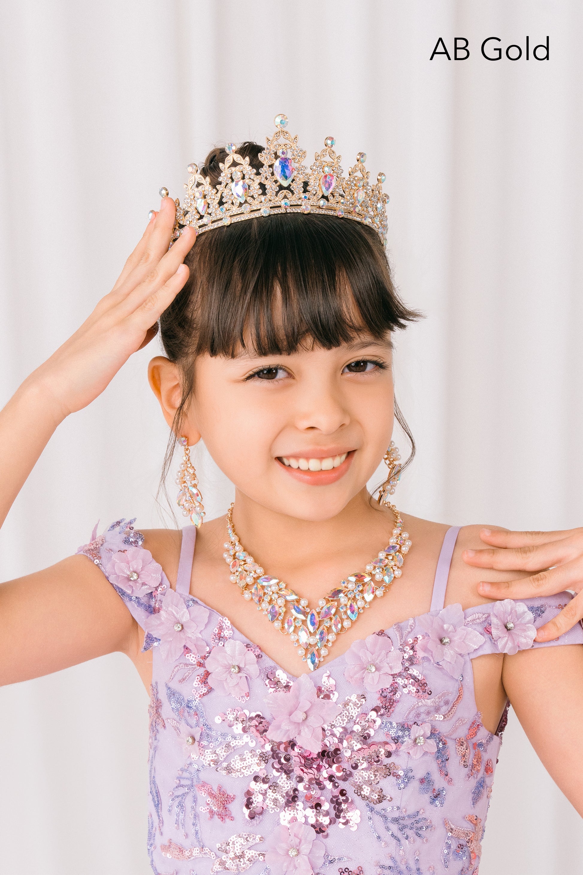 Young girl wearing a sparkling AB gold tiara and necklace against a plain background