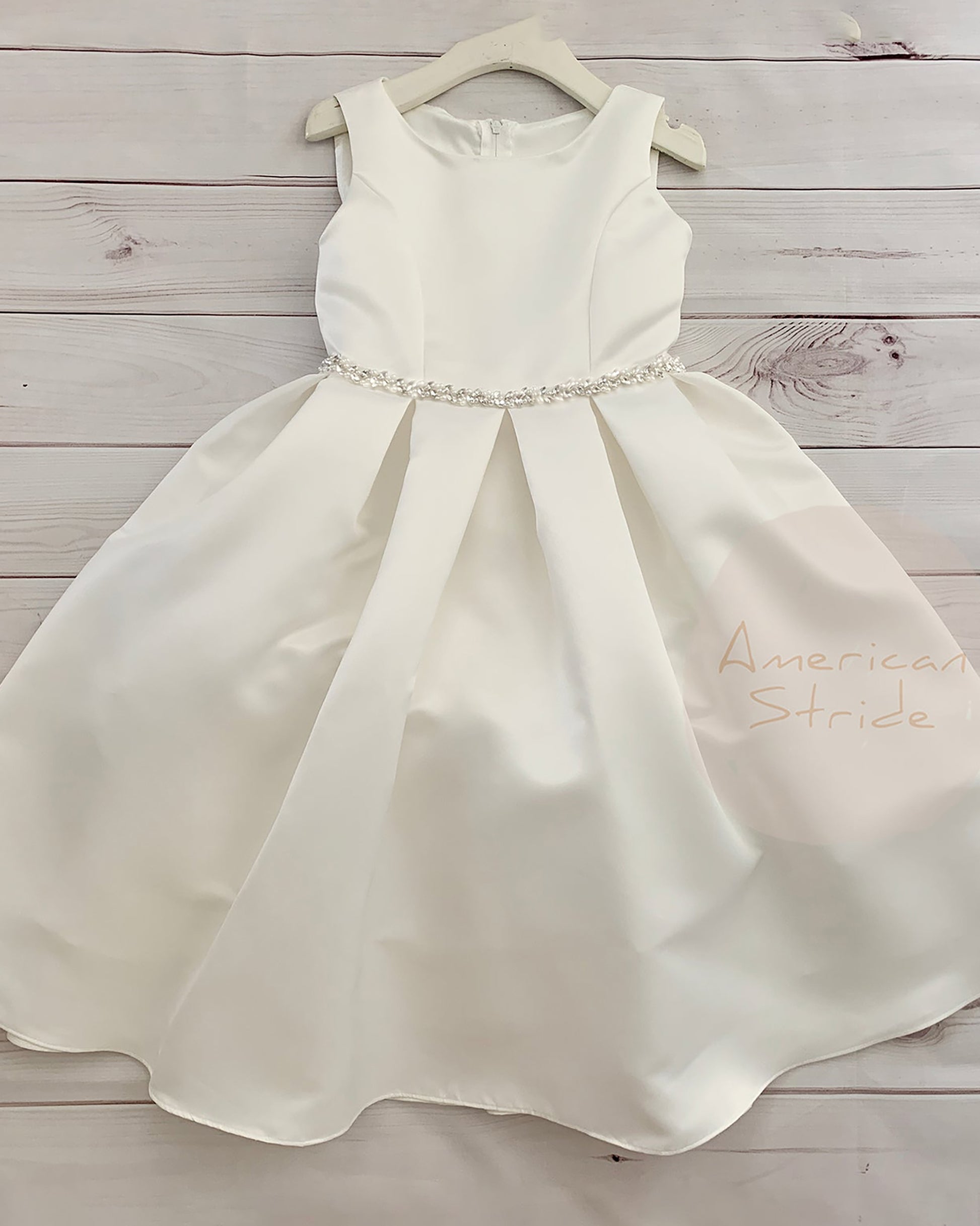 White satin dress with a beaded waistband on a wooden surface, branded 'American Stride'.