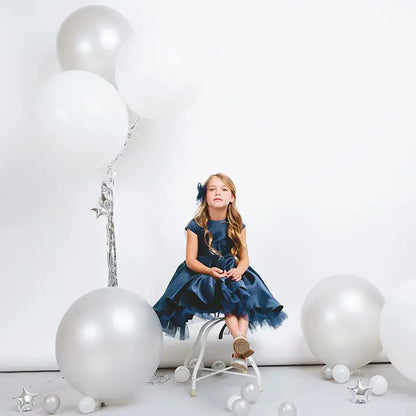 Young girl in a blue dress sitting on a stool with large white balloons around her.