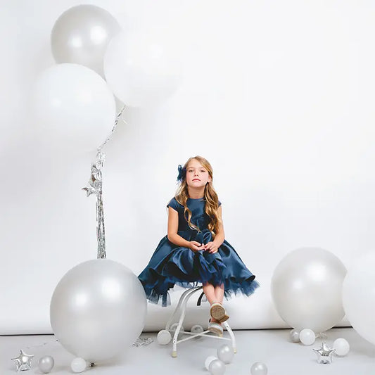 Young girl in a blue dress sitting on a stool with large white balloons around her.