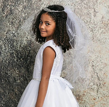 Young girl in a white dress with a veil against a textured wall.