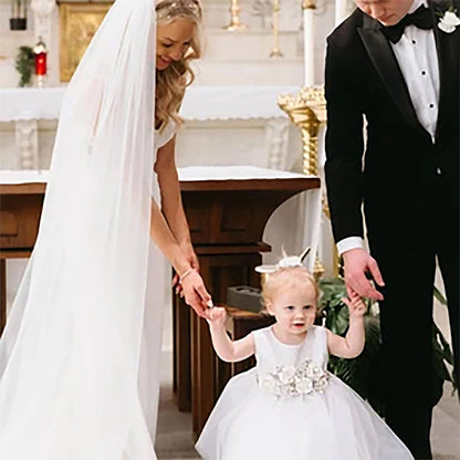 Woman in wedding dress and man in tuxedo holding hands with a young girl in a white dress in a church setting.