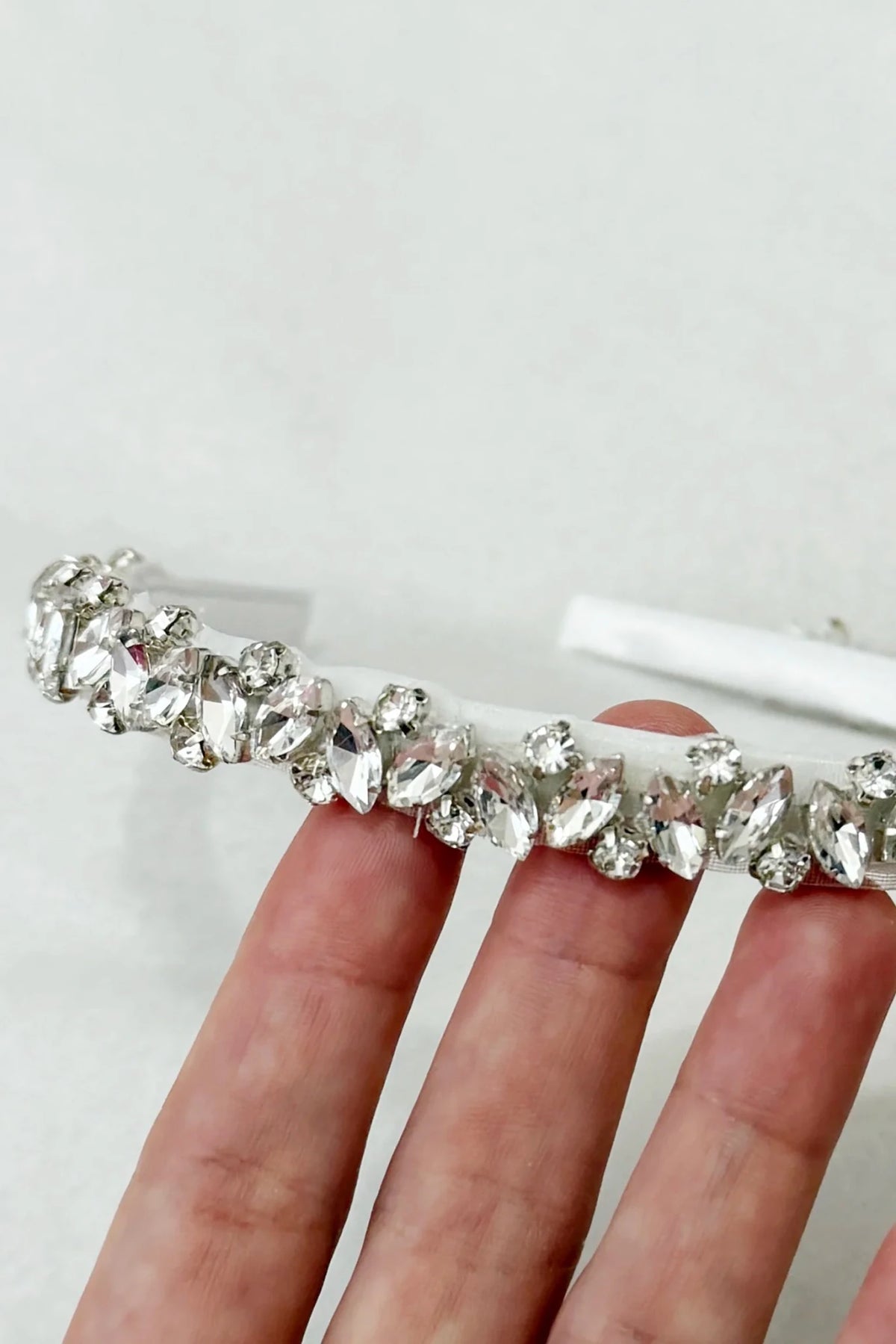 A close-up of a hand holding a clear rhinestone headband