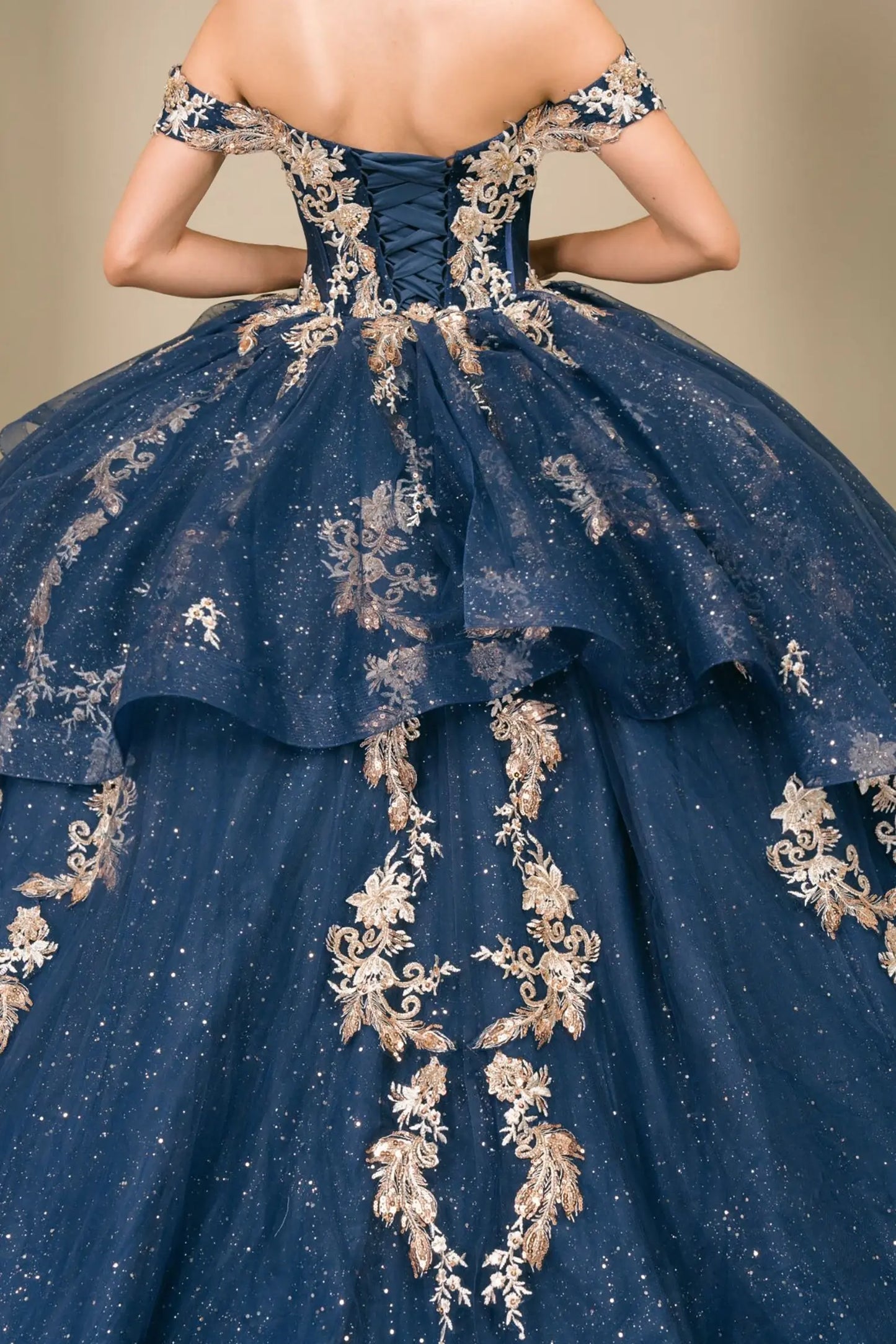 Close-up of woman back-facing in navy quinceañera dress with lace-up corset bodice, gold embroidery, detachable cape layer, and extended train detail