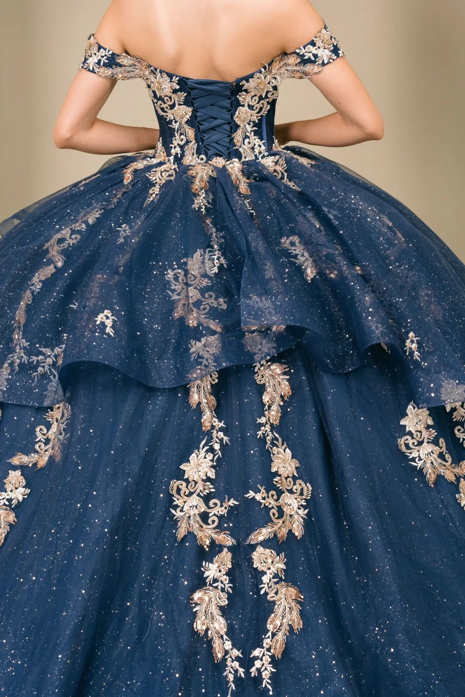 Close-up of woman back-facing in navy quinceañera dress with lace-up corset bodice, gold embroidery, detachable cape layer, and extended train detail