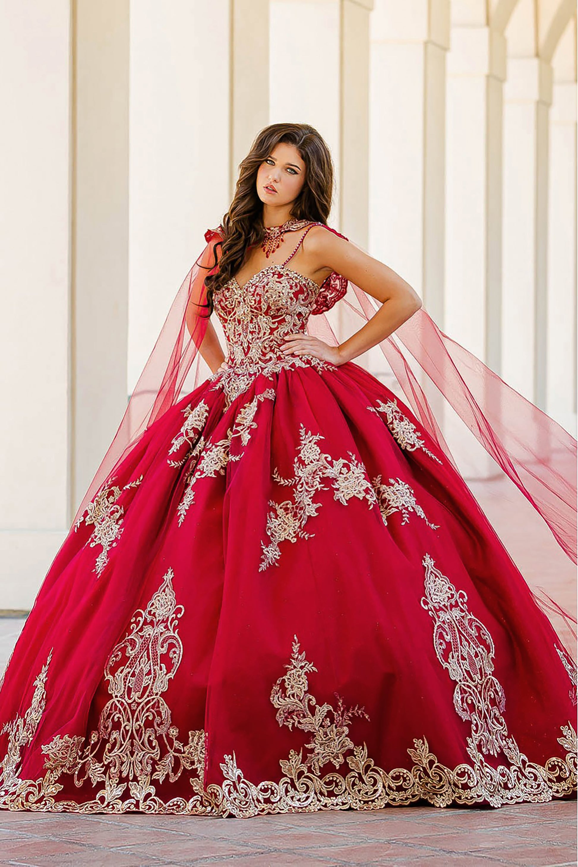 Quinceanera | Wine with Gold Embroidered Lace with Stunning Cape Quince Ballgown dress - front view of woman wearing dress with both hands at her hips and a serious look on her face