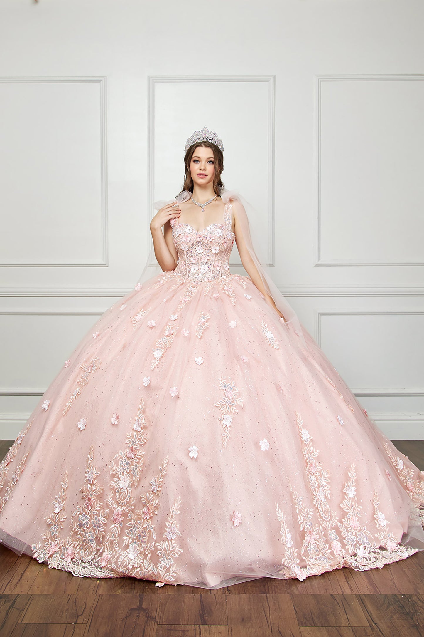 Quinceanera | Blush-Peach Flower Embroidery, Gem Detailing, and glitter lining Quince Ballgown with Tulle Shoulder Drape - front view of woman wearing dress with one hand near shoulder and the other hand at her side