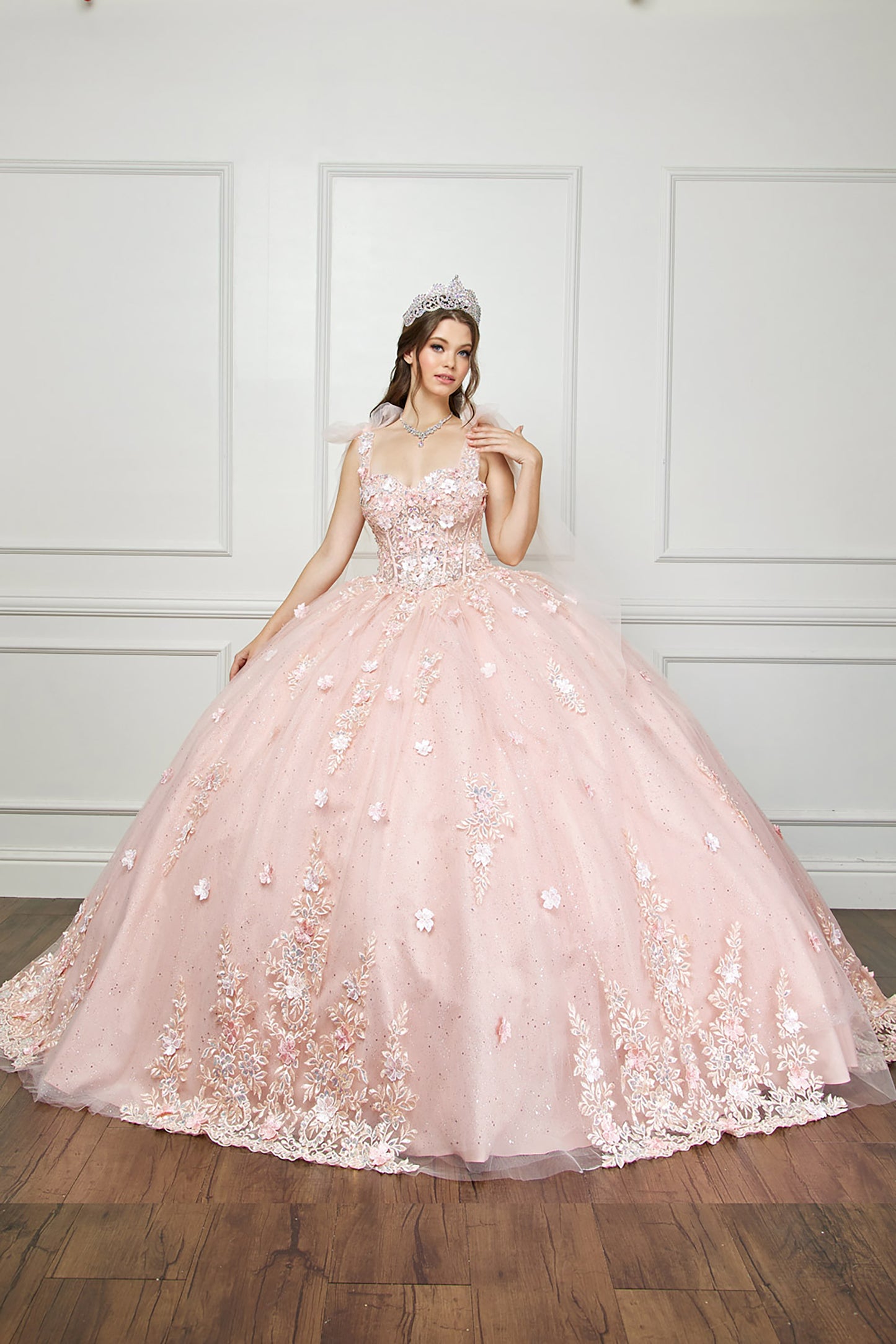 Quinceanera | Blush-Peach Flower Embroidery, Gem Detailing, and glitter lining Quince Ballgown with Tulle Shoulder Drape - front view of woman wearing dress with one hand on her shoulder