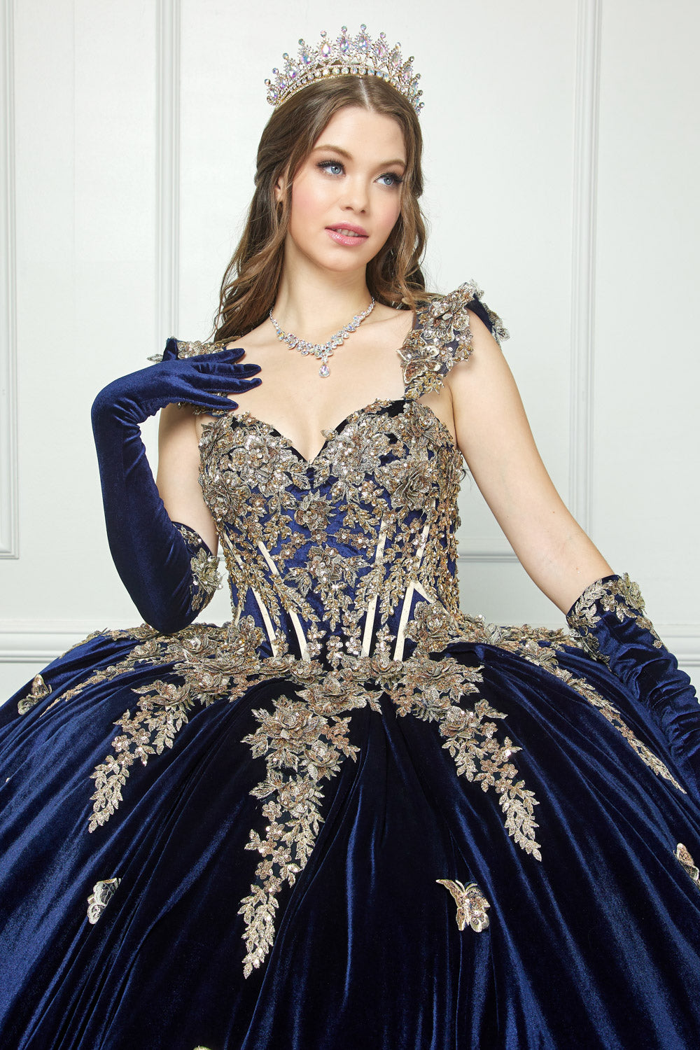 Navy Quinceanera | Off-shoulder Velvet Sweetheart Gold Sequin sequin butterfly floral Ballgown with Sweep train - front zoomed in view of woman wearing dress and crown looking off to the side