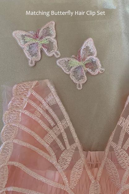 A close-up of a pale pink embroidered butterfly hair clip set placed on a soft beige fabric background