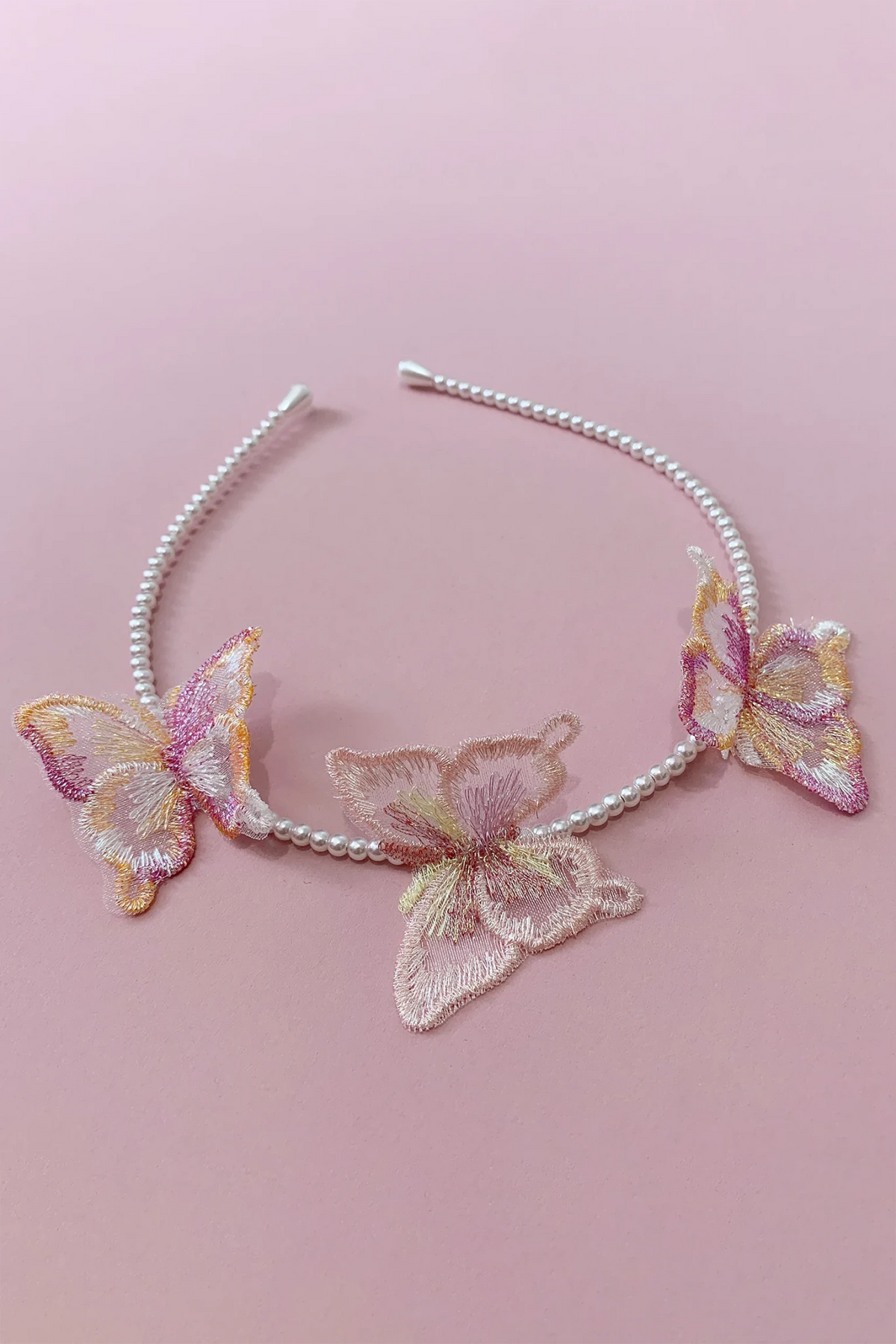A silver and white beaded headband decorated with three embroidered butterfly appliqués in pastel pink, gold, and cream