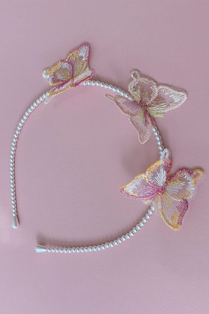 A white beaded headband decorated with three embroidered iridescent butterflies in pink, yellow, and beige