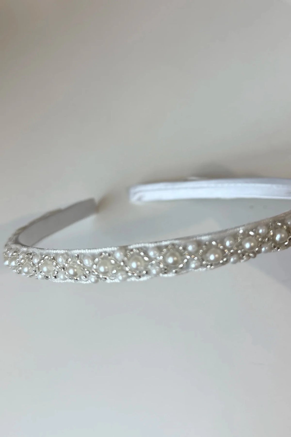 Intricate features stand out across ivory pearl headband with satin fabric.