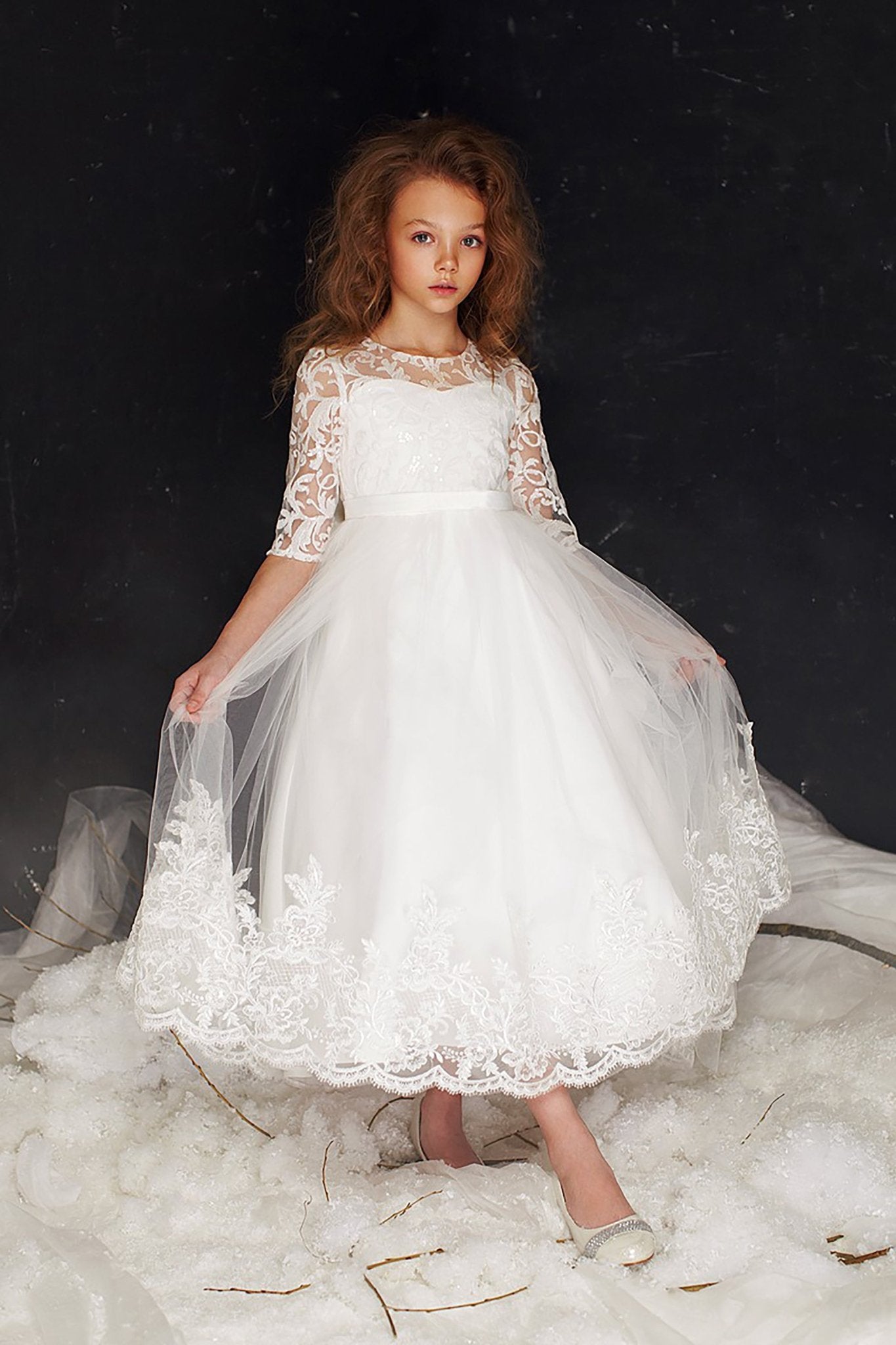 Front view of a white communion dress with three-quarter floral lace sleeves, an embroidered bodice, and a lace-trimmed high-low tulle skirt.