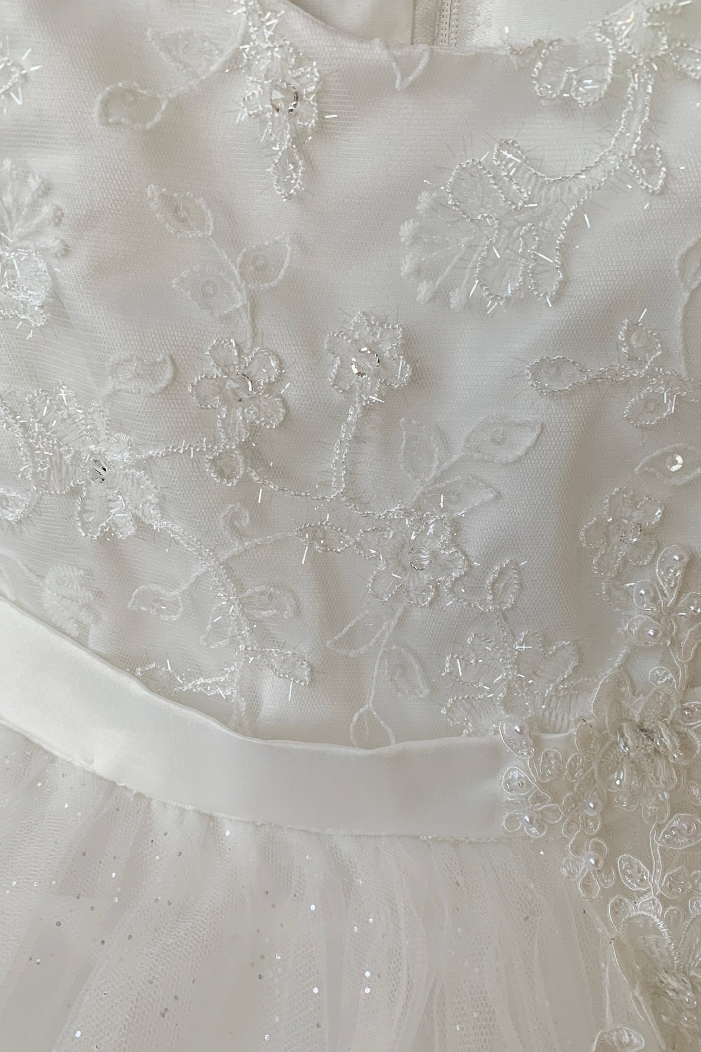 Close-up of a white flower girl dress with intricate lace and beadwork. Also suitable as a communion dress.