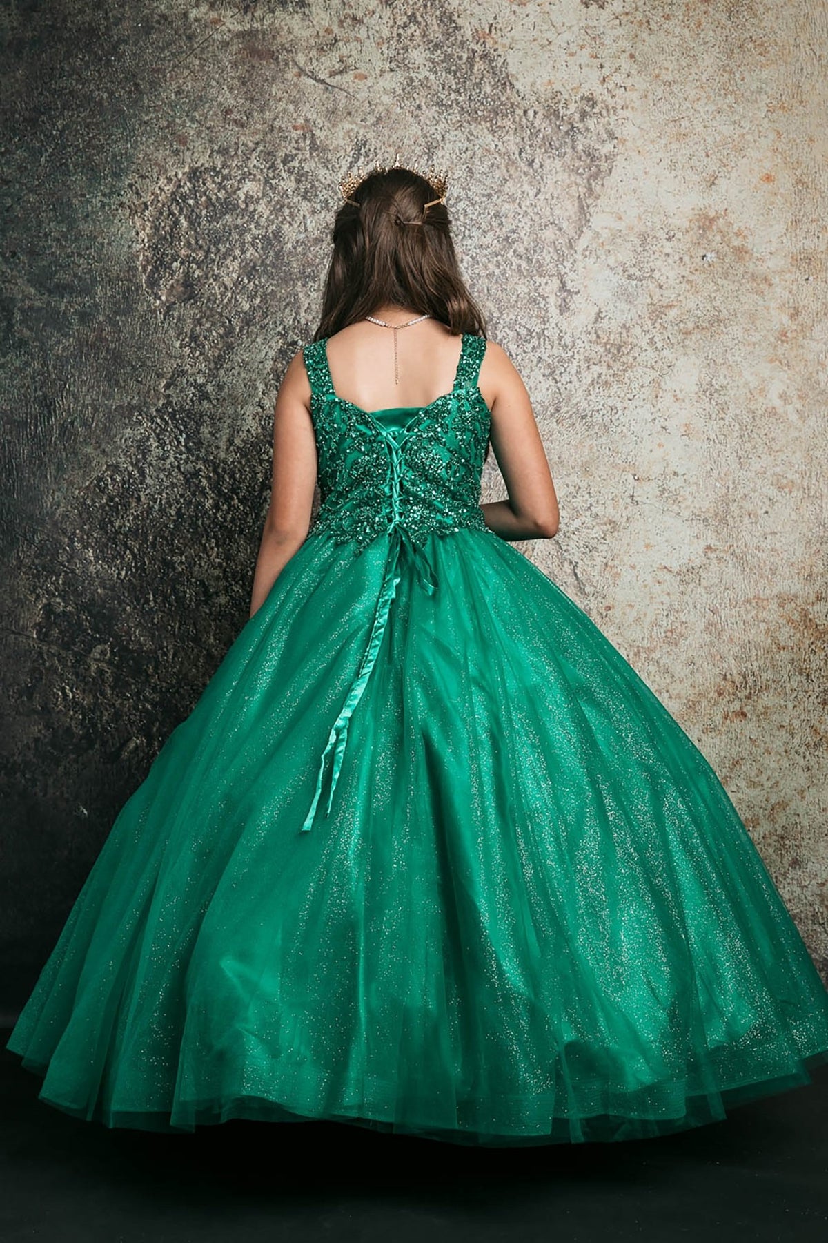 Back view of a green kids mini quinceanera mini quince dress with lace-up corset, oversized bow, sequin beaded bodice, and glitter tulle train.
