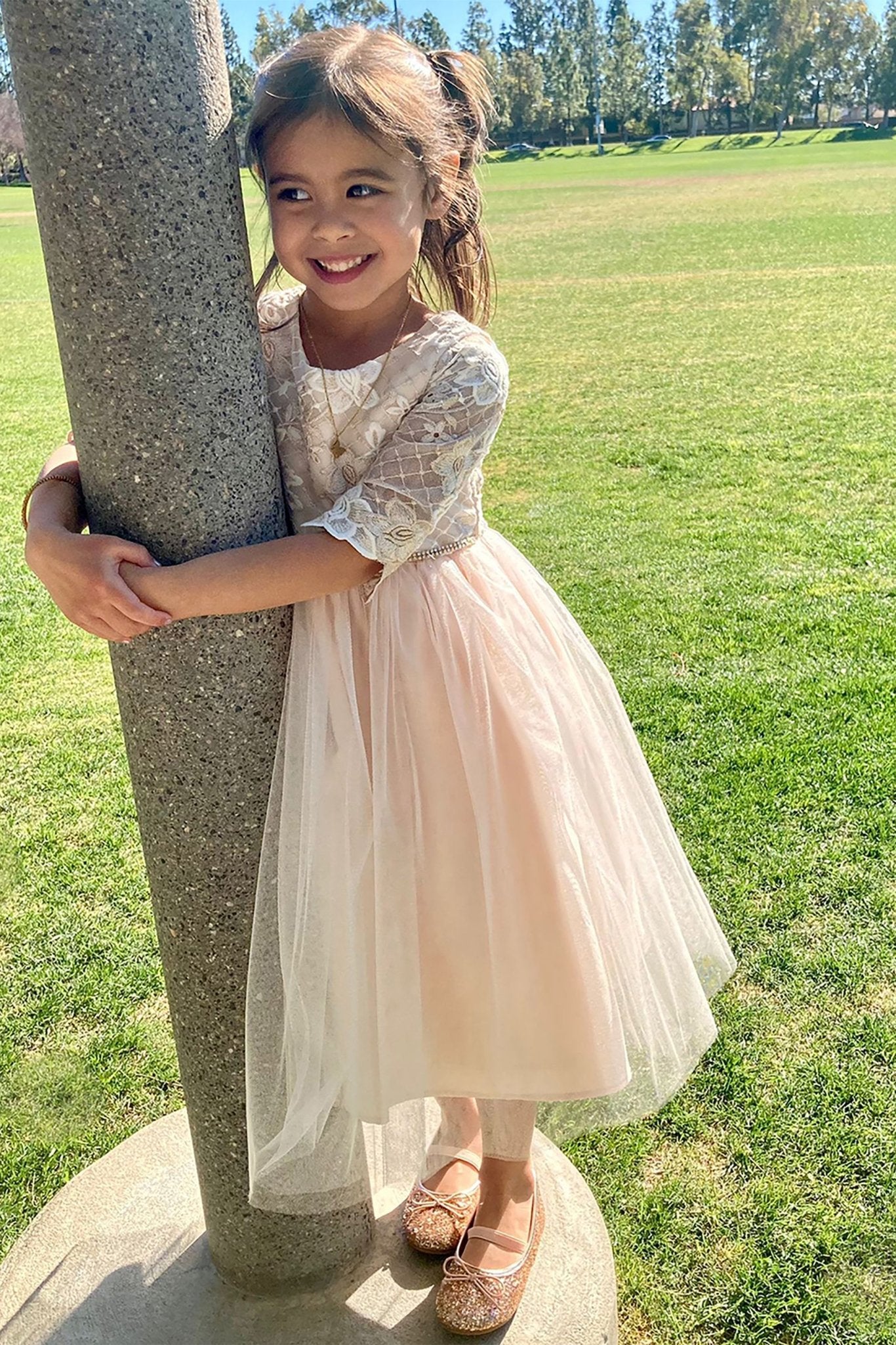 Young girl in a champagne dress standing next to a tree in a park