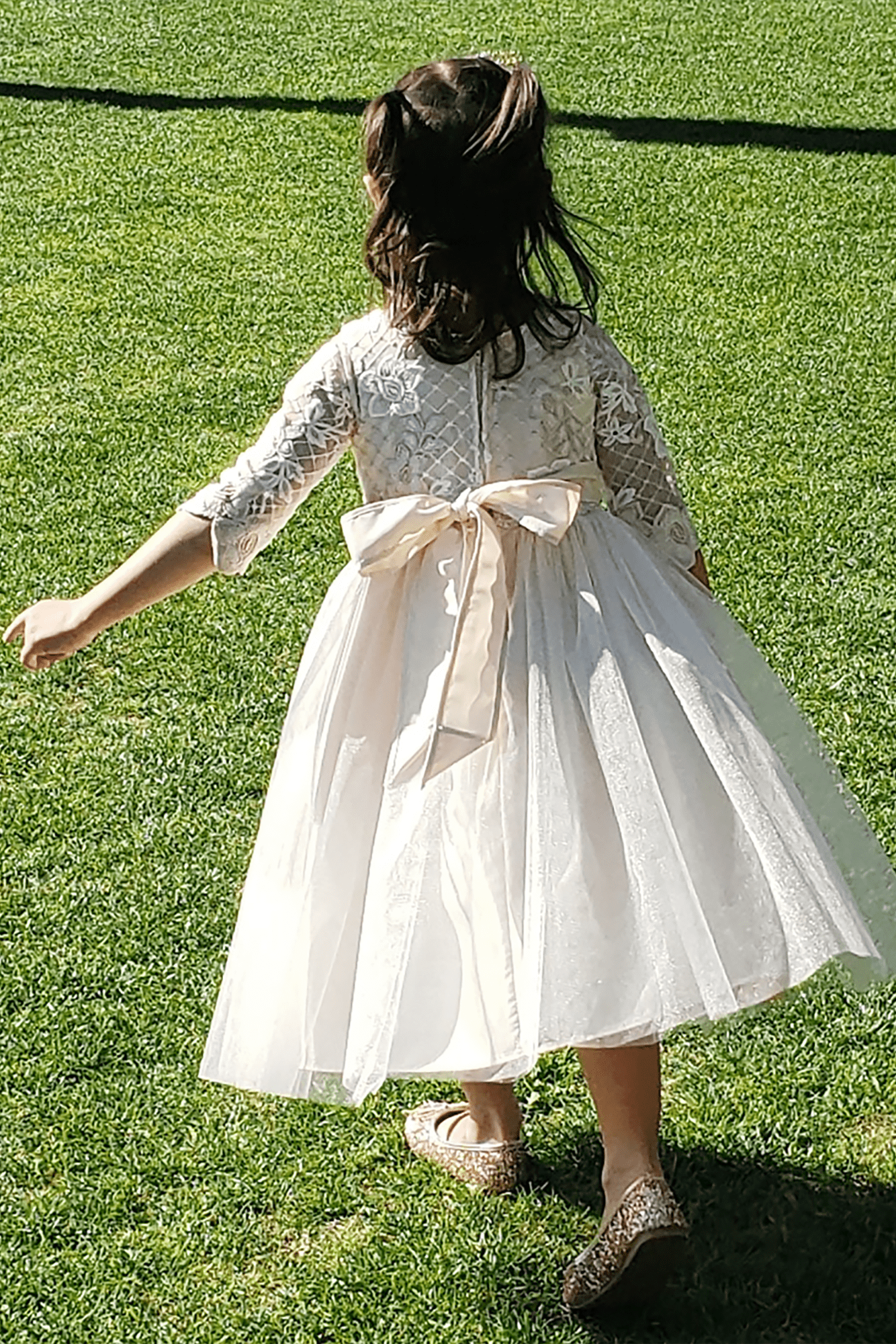 Child in a champagne dress with a large bow standing on grass