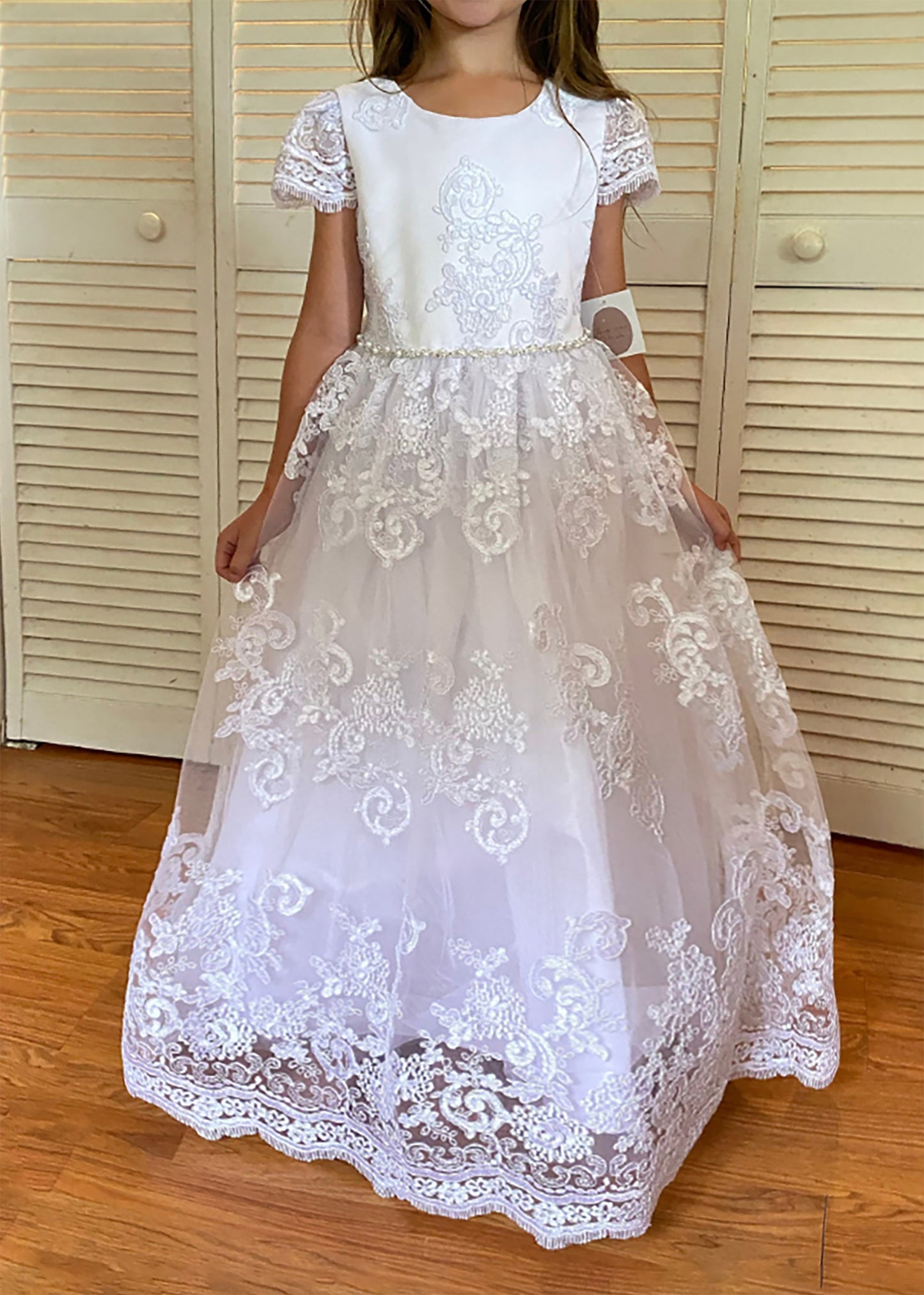 White lace dress worn by a person in front of a wooden door.