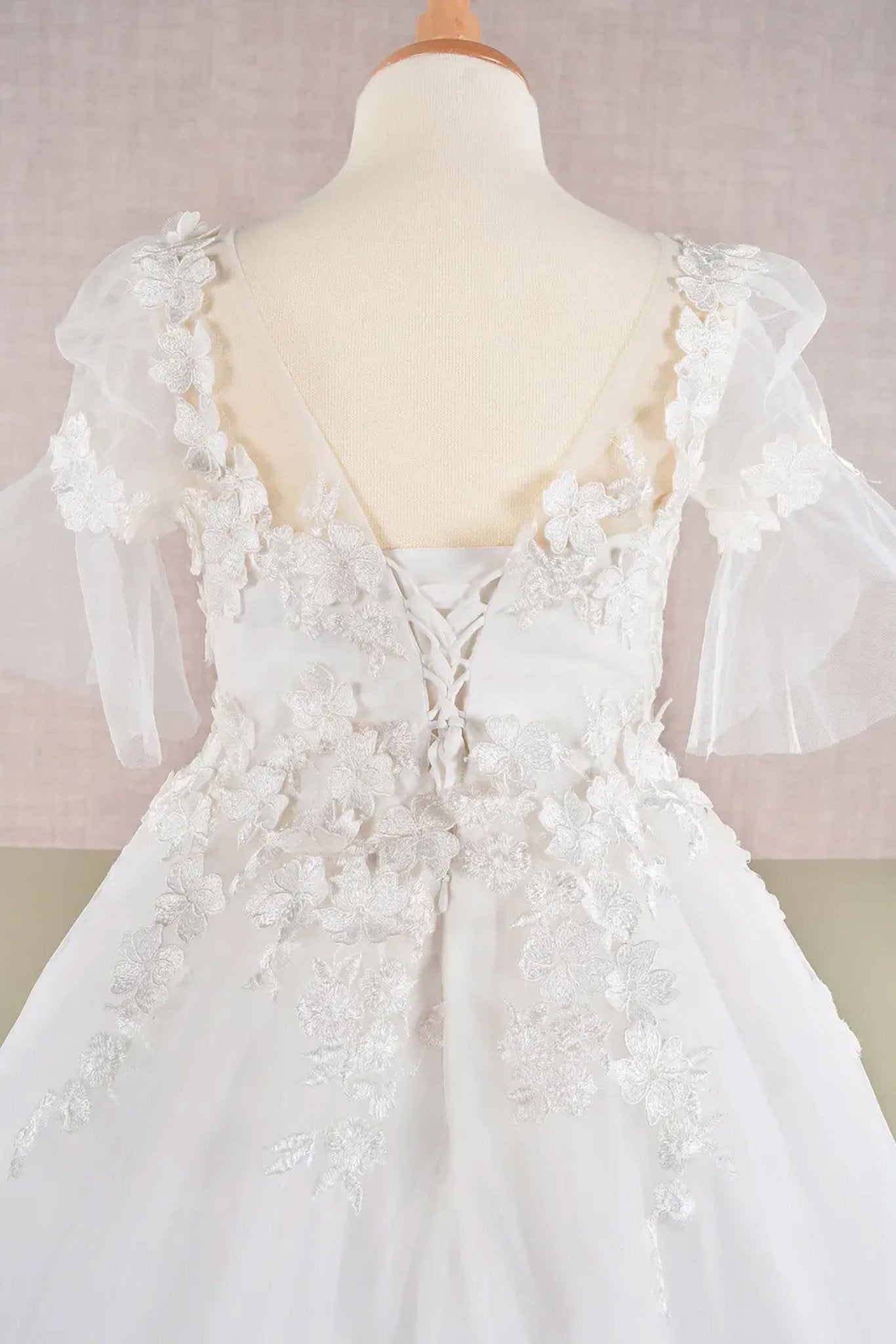 Close up view of back off-white kids mini quinceañera flower girl dress highlighting 3D floral appliques, mesh overlay and puff sleeve design and lace back up. Also suitable as a mini quince dress. Also suitable as a communion dress.