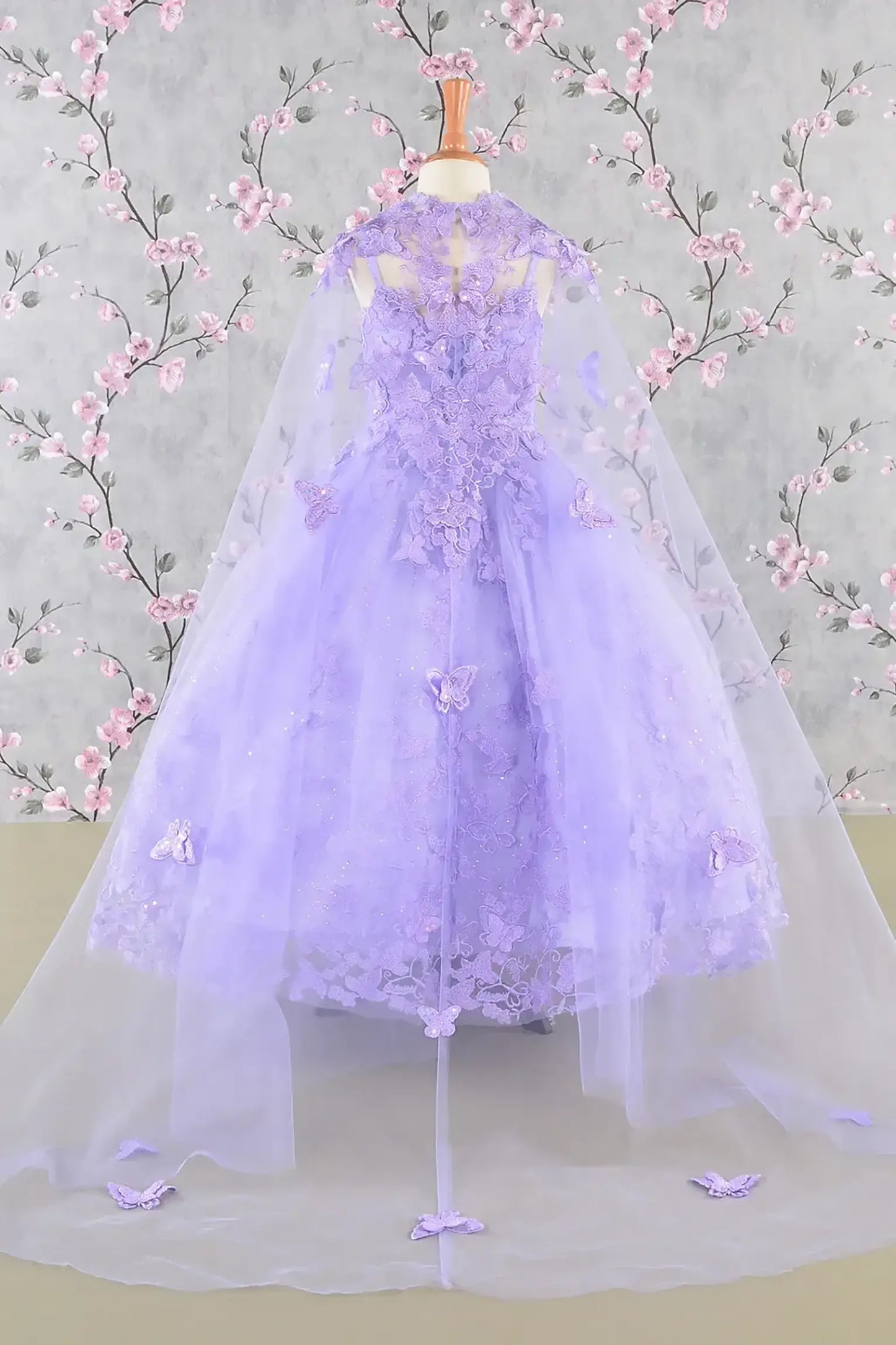Back view of a lilac kids ball gown with 3D butterflies, sequins, and detachable mesh cape