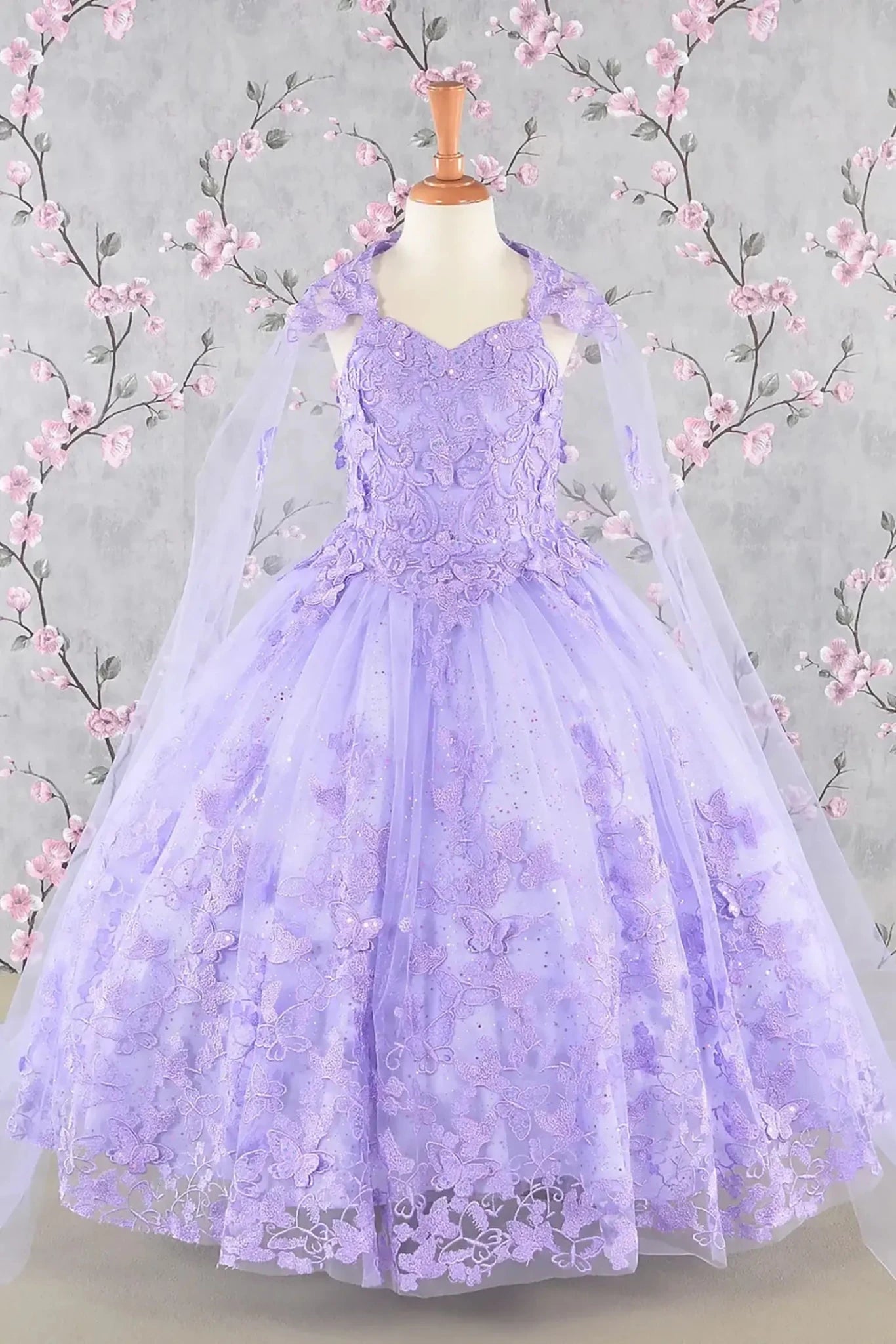Front view of lilac kids mini quinceañera mini quince dress with 3D butterfly appliques, sequin-embellished bodice, glitter tulle skirt, and flowing mesh cape.