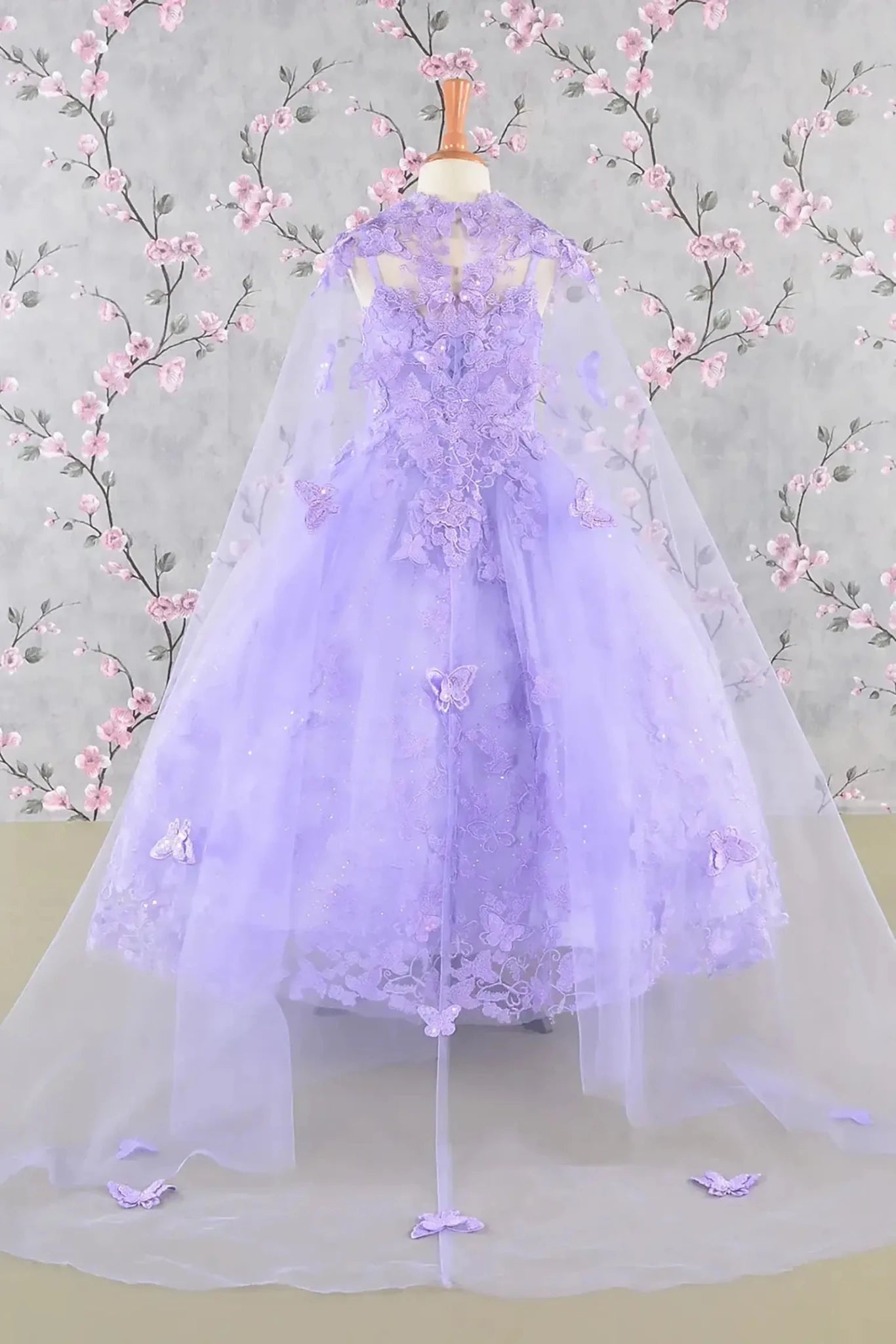 Back view of a lilac kids mini quince dress with 3D butterflies, sequins, and detachable mesh cape.