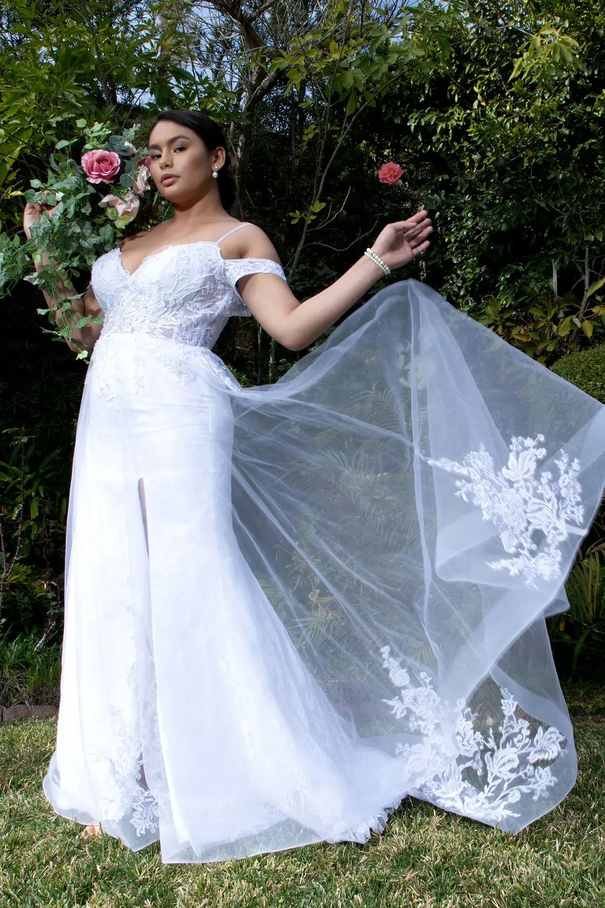 White wedding gown with a sheer embroidered overlay spreading from its fitted lace waist.