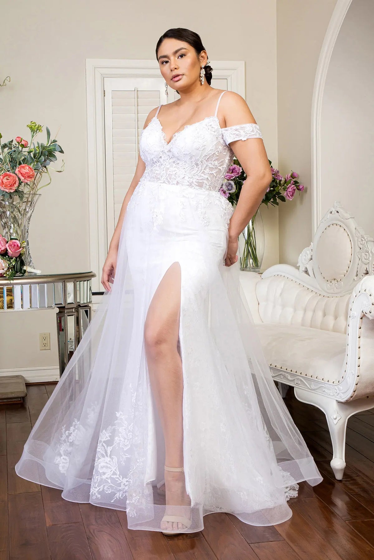Visible beneath the mesh overlay, a front slit opens the fitted lace skirt of this white wedding gown.