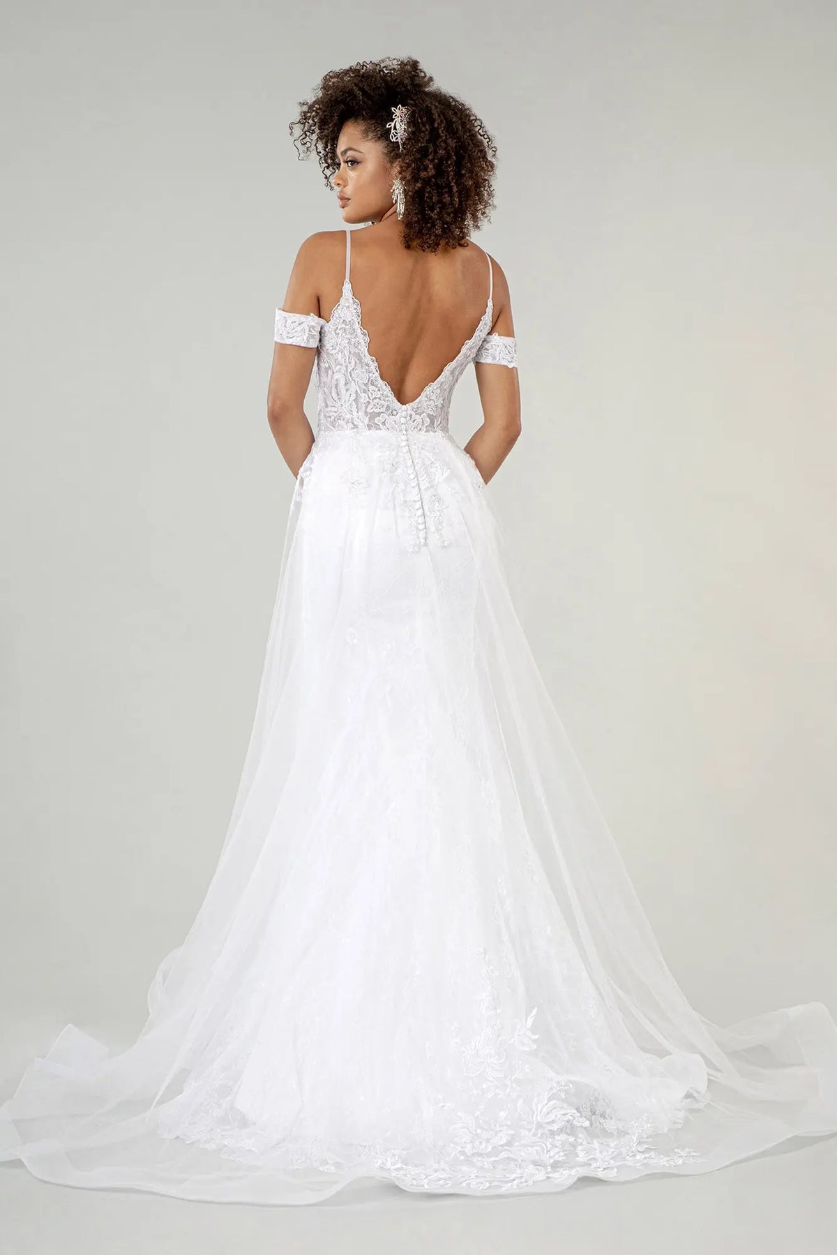 The white wedding gown's long lace-edged overlay extends below an open V-back.