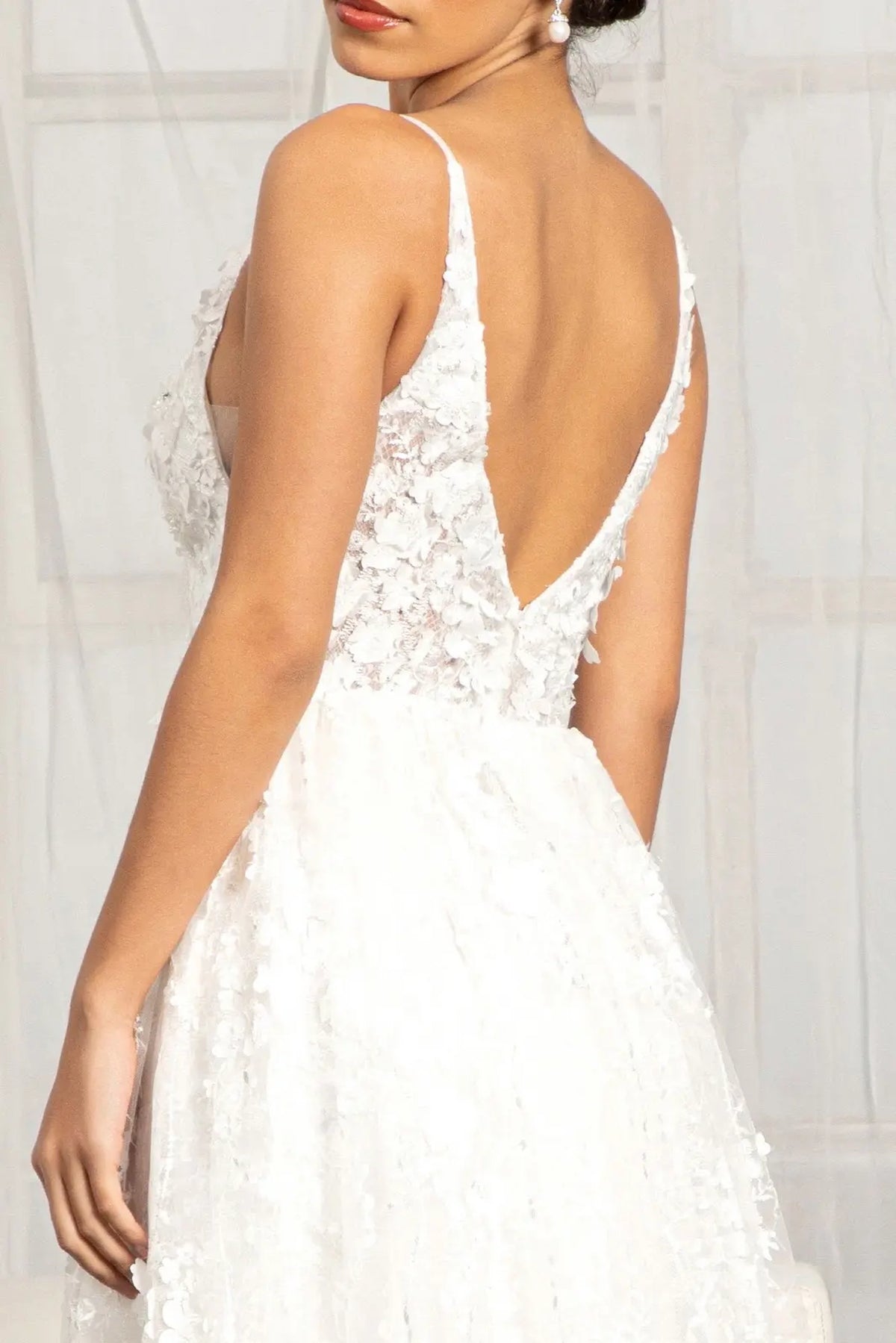 White wedding gown showing its deep V-back and sheer floral-embroidered bodice.