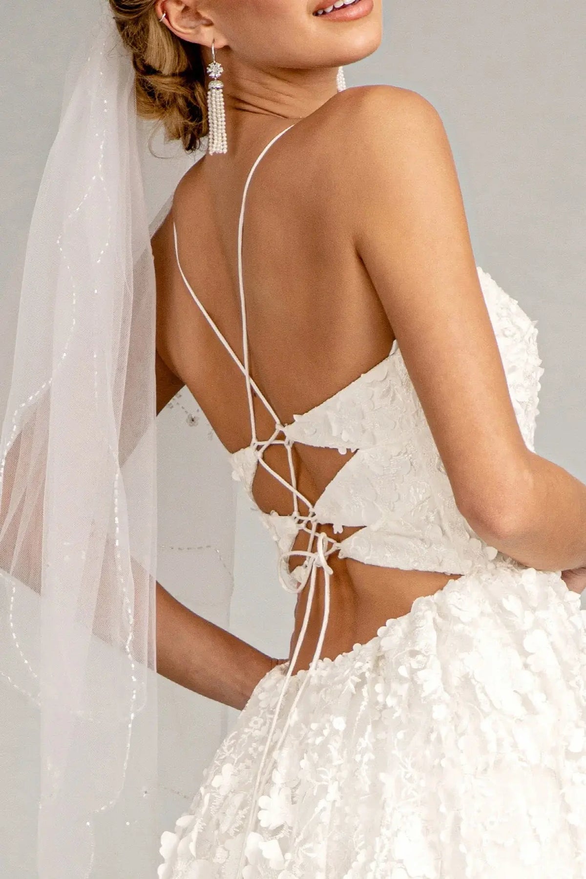 Ribbon lacing connects the open back of this white wedding gown beneath fine straps.